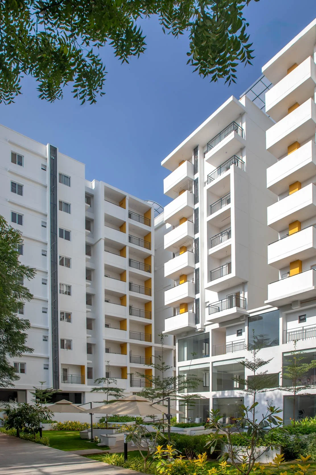 Exterior real estate photography showcasing a contemporary mid-rise apartment building, highlighting modern glass facades, clean white architecture, and a clear blue sky