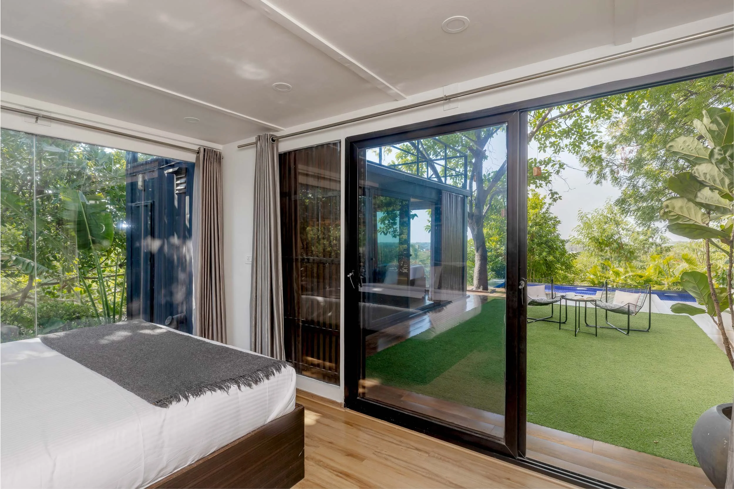 Exterior twilight photography of a modern luxury staycation in Hyderabad, featuring a covered outdoor deck with comfortable wicker seating, warm ambient lighting, and wooden slatted privacy screens