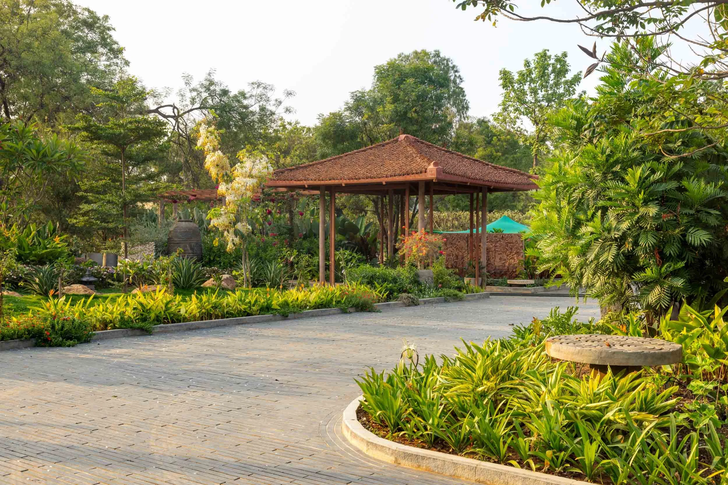 A paved circular driveway leading to a traditional tiled-roof pavilion, surrounded by manicured green lawns and lush tropical landscaping.