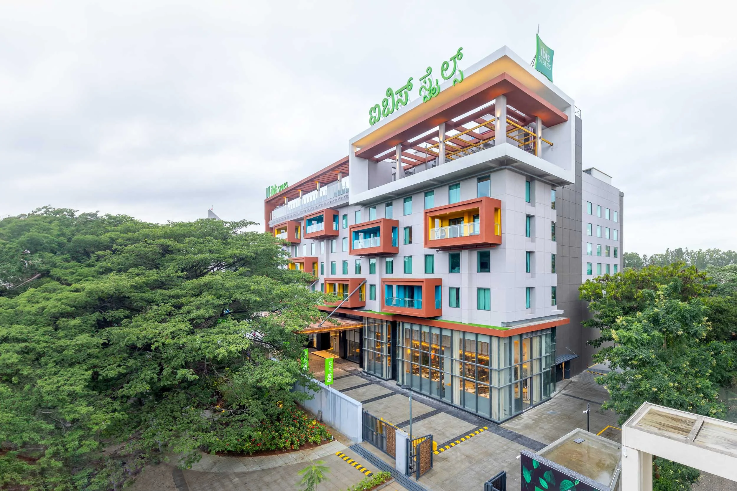 Exterior photography of a modern hotel building featuring a white facade with bright orange architectural accents, surrounded by lush green trees