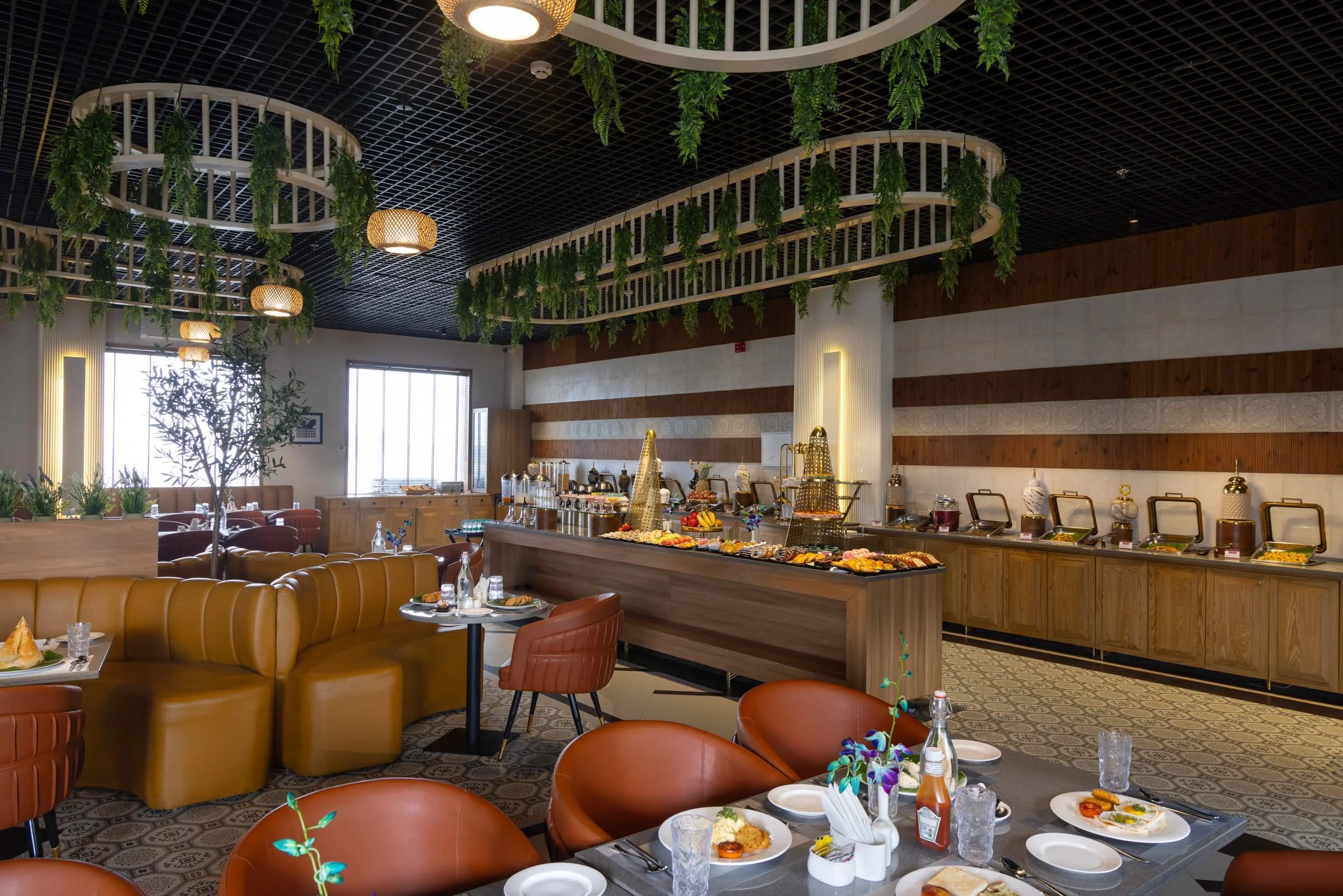Interior photography of a modern hotel restaurant featuring hanging ceiling plants, mustard banquette seating, round orange chairs, and large windows