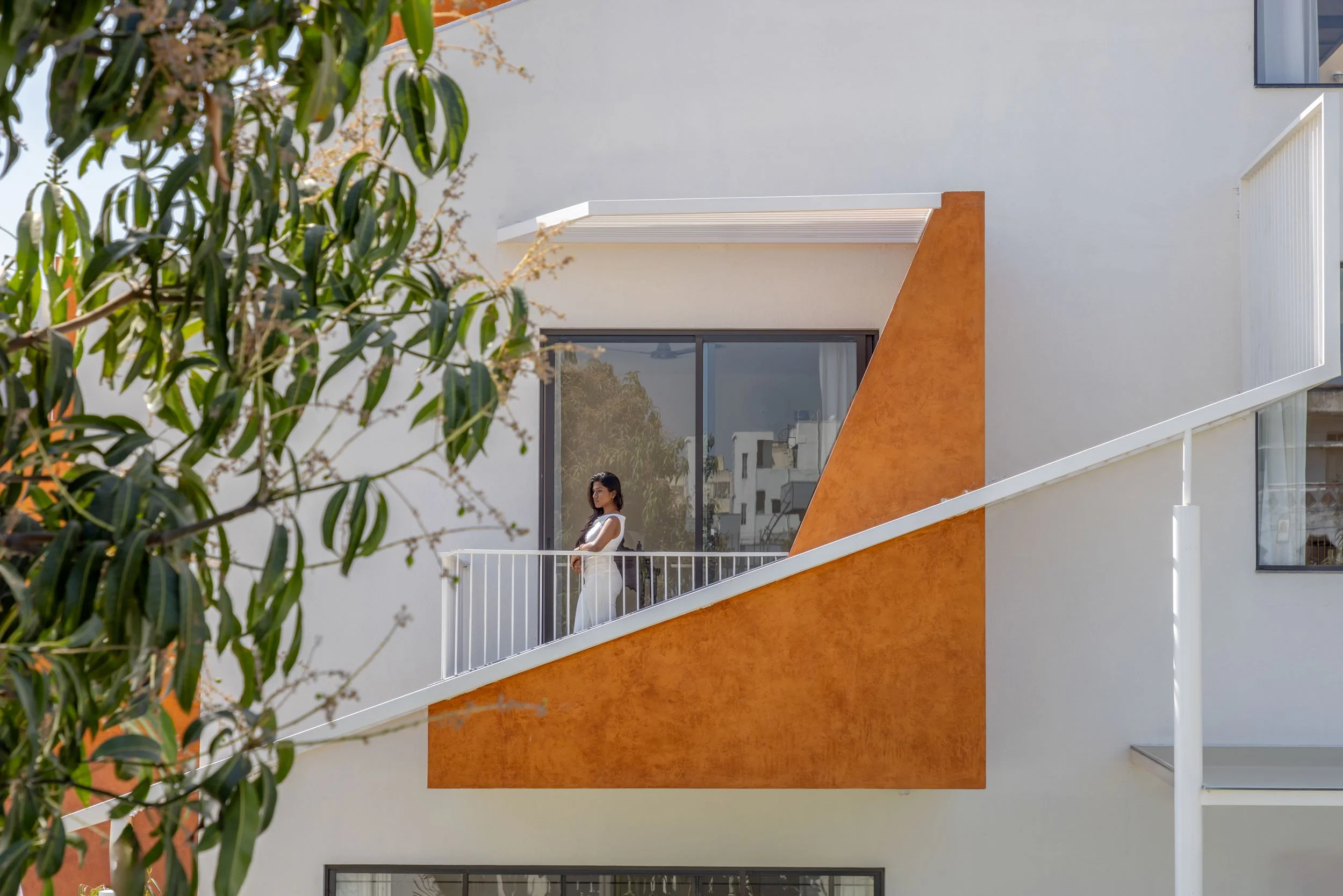 Professional exterior architectural photography of a modern residential home, framing a striking terracotta-accented balcony with natural greenery