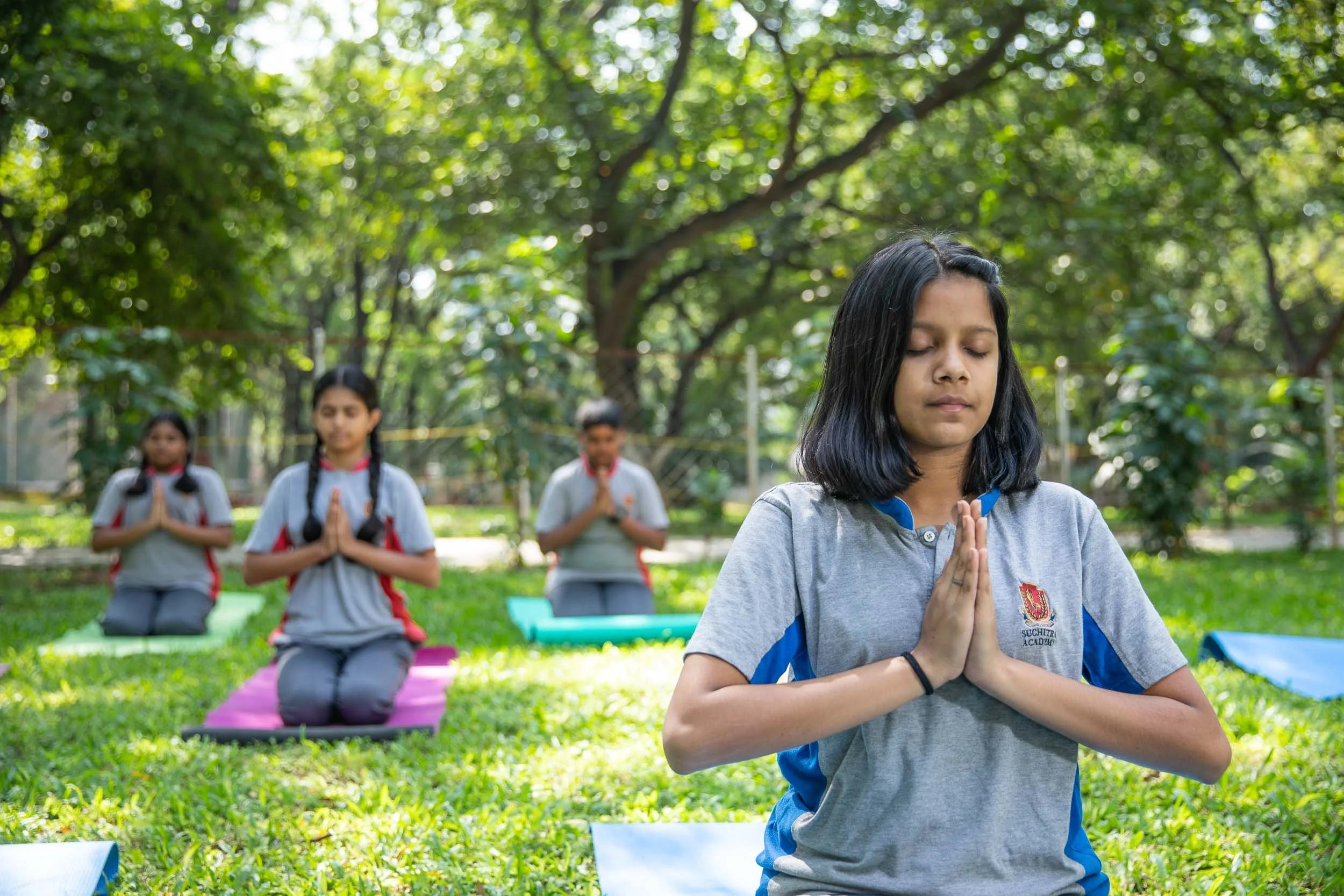 Exterior school photography of students practicing yoga and meditation in a lush green campus environment