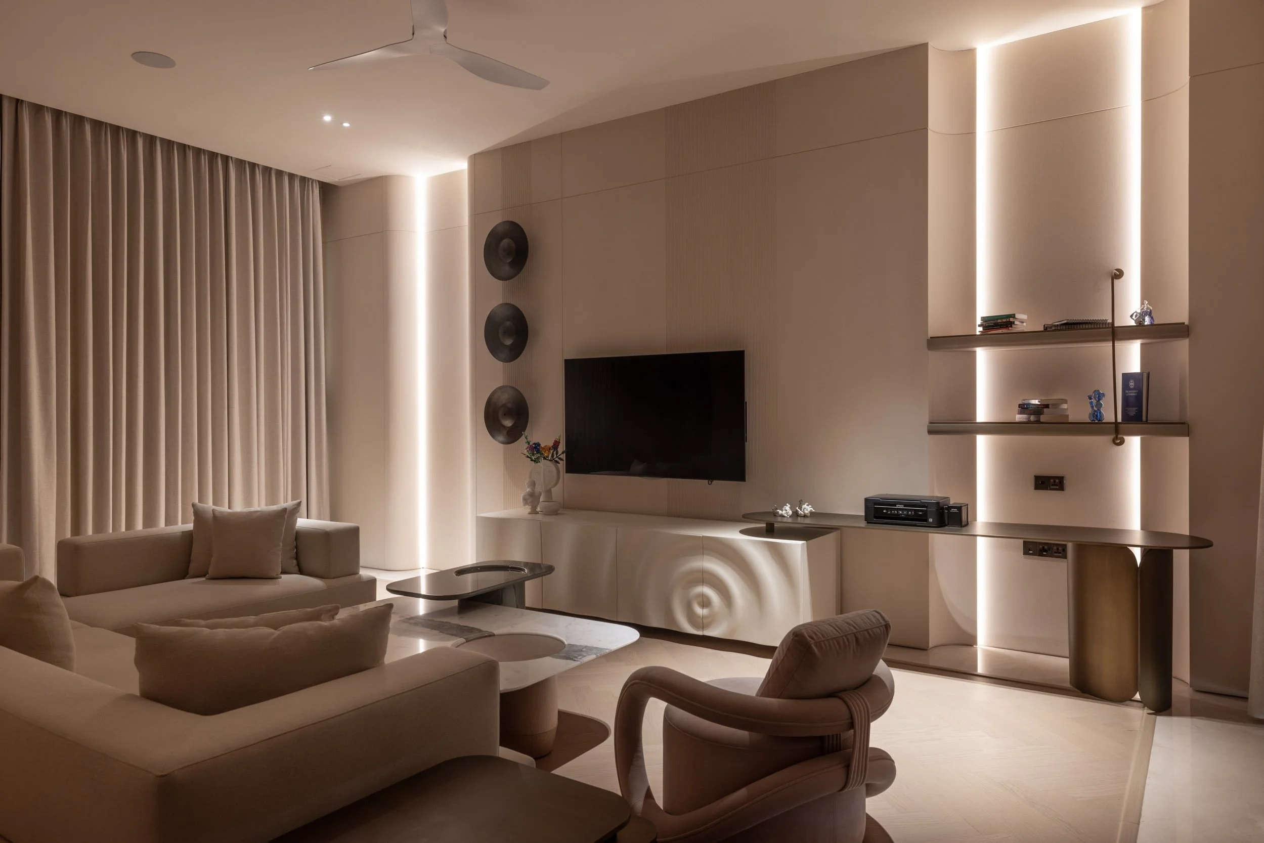 Modern residential interior featuring warm vertical architectural lighting, a wall-mounted TV, and contemporary lounge seating