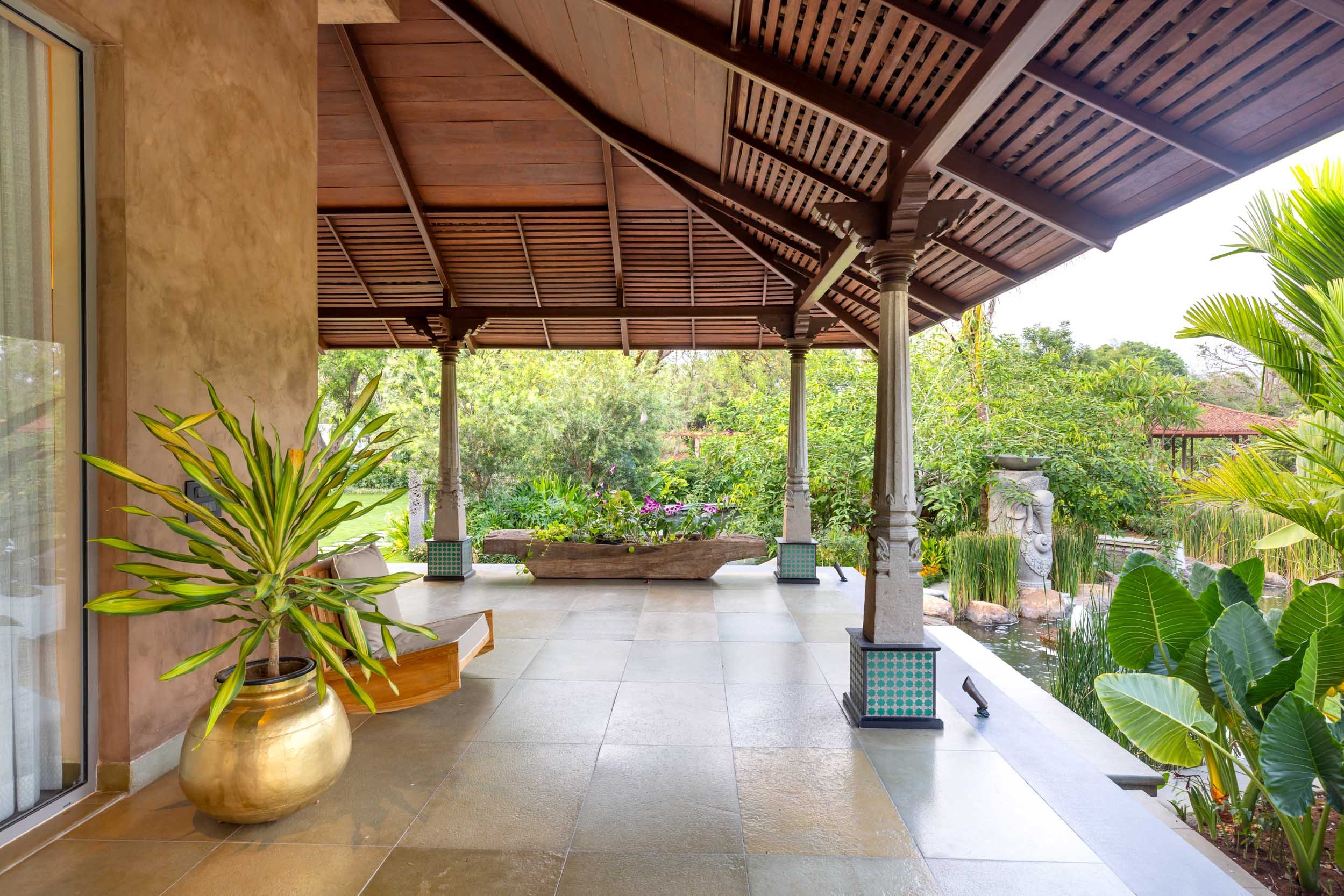 An outdoor residential courtyard featuring a vibrant blue textured accent wall, a small tree, potted plants, and stone flooring