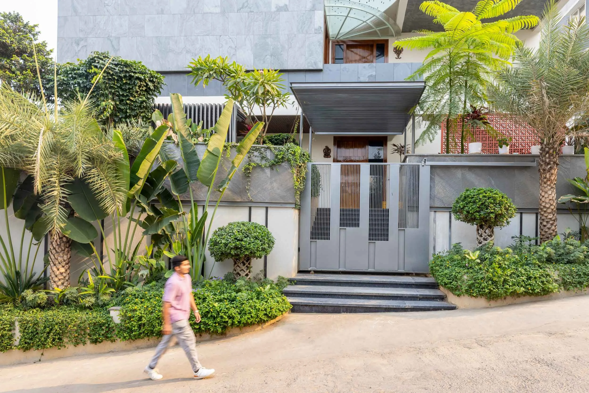 Professional exterior architectural photography of a modern residential home, highlighting a striking dark grey entrance gate and vibrant, lush landscaping