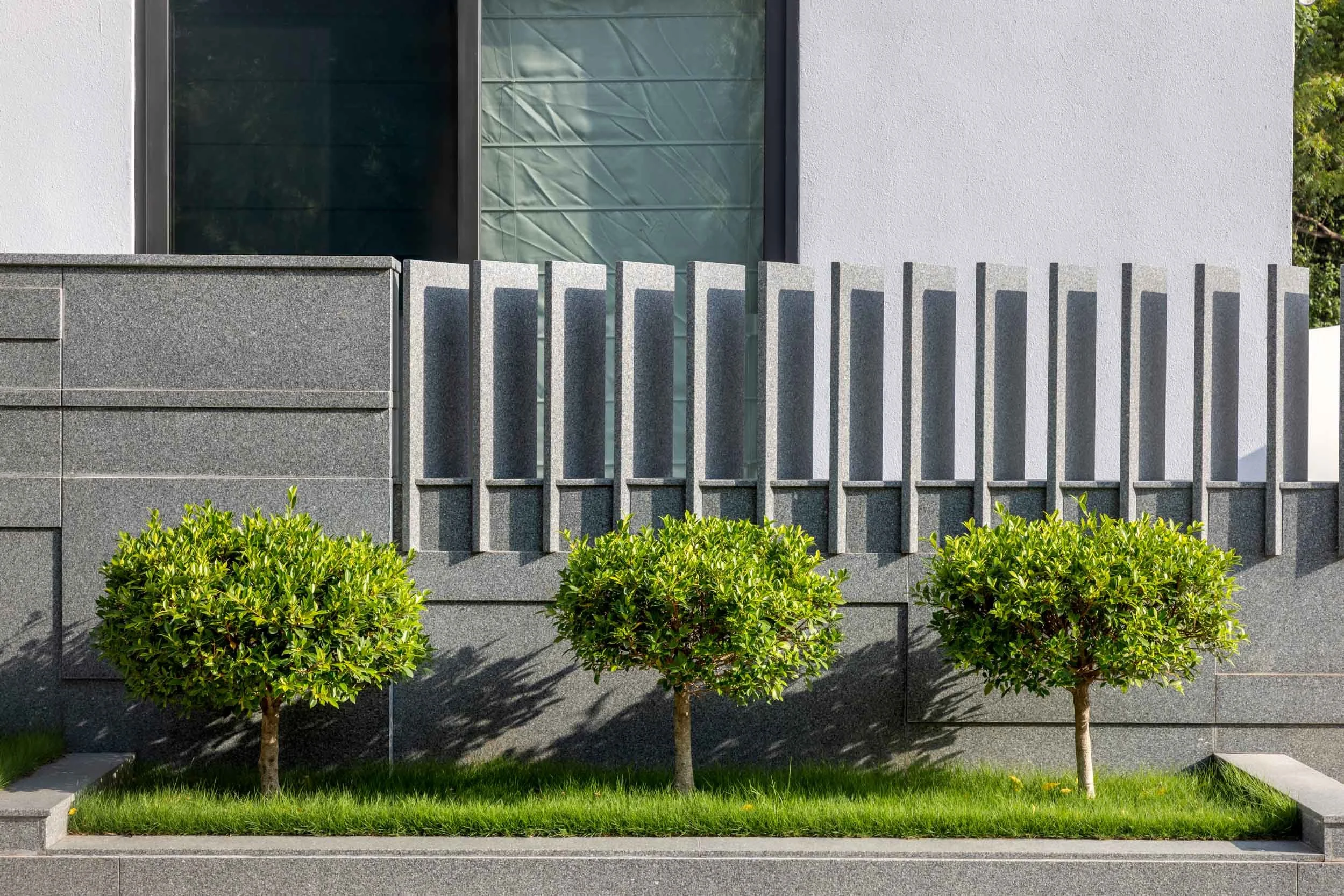 Professional exterior architectural photography of a modern residential home, highlighting a beautifully textured boundary wall with vertical slats and perfectly manicured landscaping