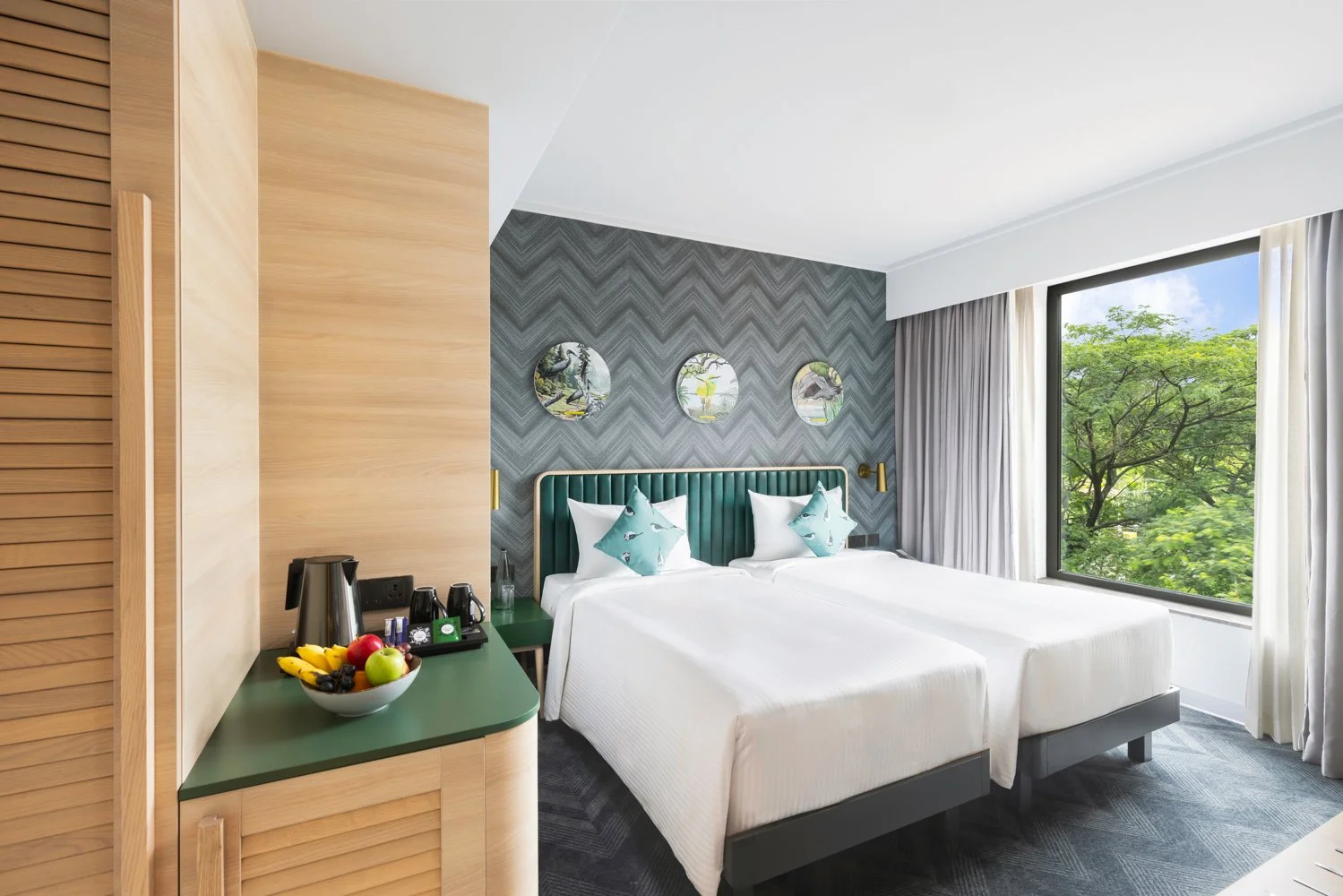 Interior photography of a modern hotel bedroom featuring a dark patterned accent wall, twin beds with teal accents, light wooden cabinetry, and a large window with nature views