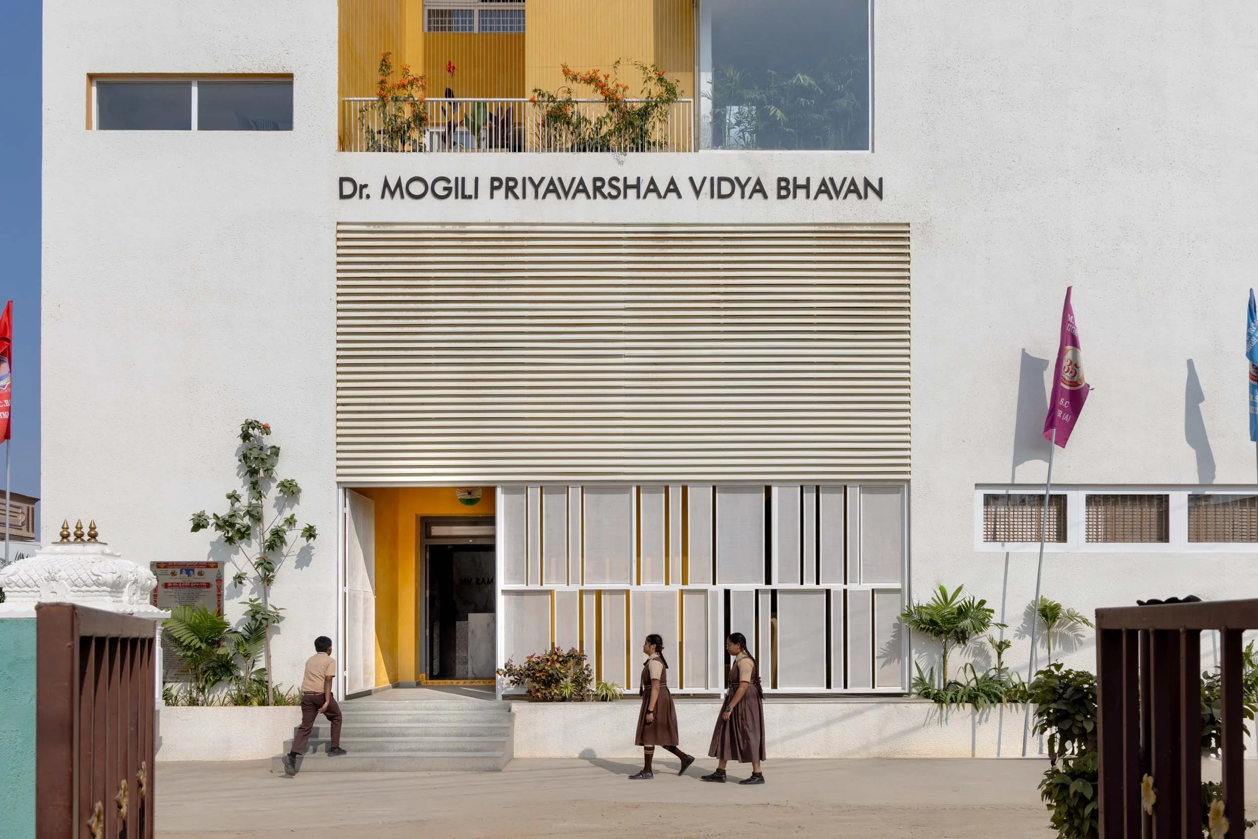 Professional architectural photography of a modern educational institution, highlighting a clean facade, vibrant yellow entrance pillars, and a wide, welcoming staircase