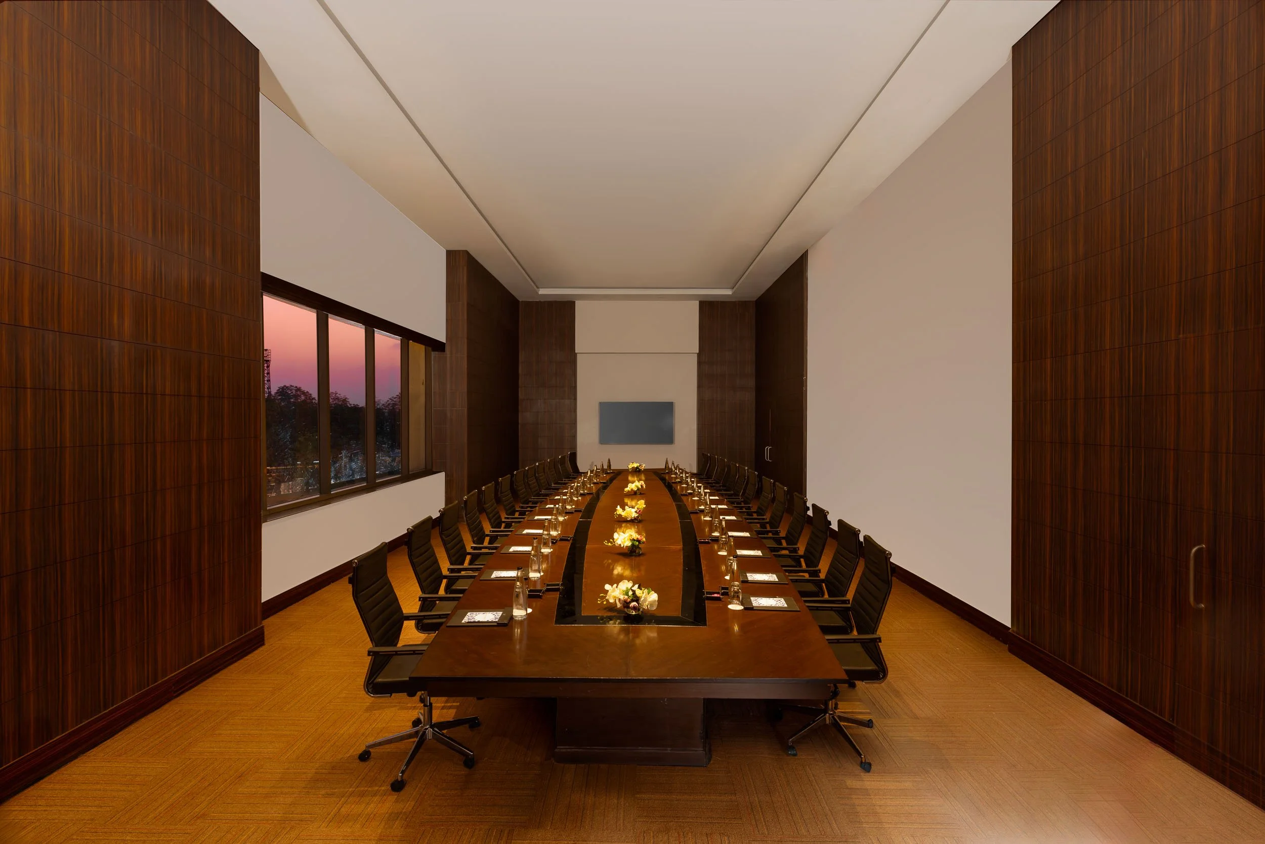 Interior photography of an exclusive hotel private dining room featuring a long dark wood table, formal place settings, wooden flooring, and warm ambient lighting