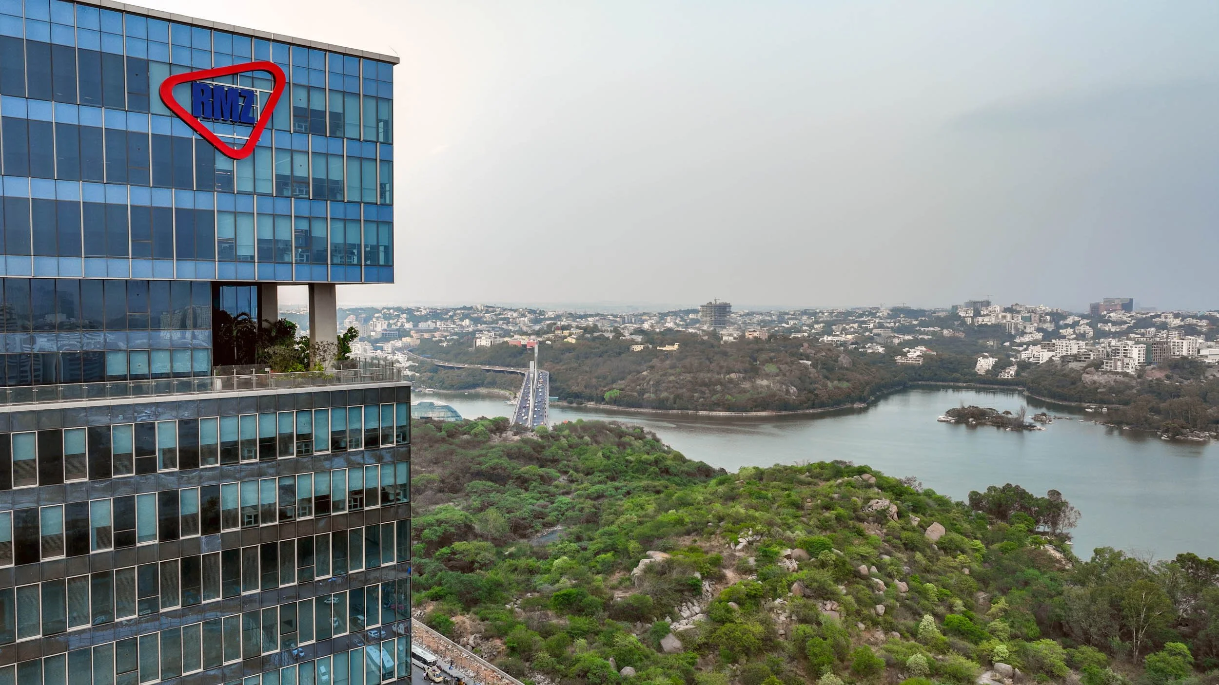 Professional aerial architecture photography capturing a modern commercial office building, highlighting its sleek blue glass facade and scenic lakeside surroundings