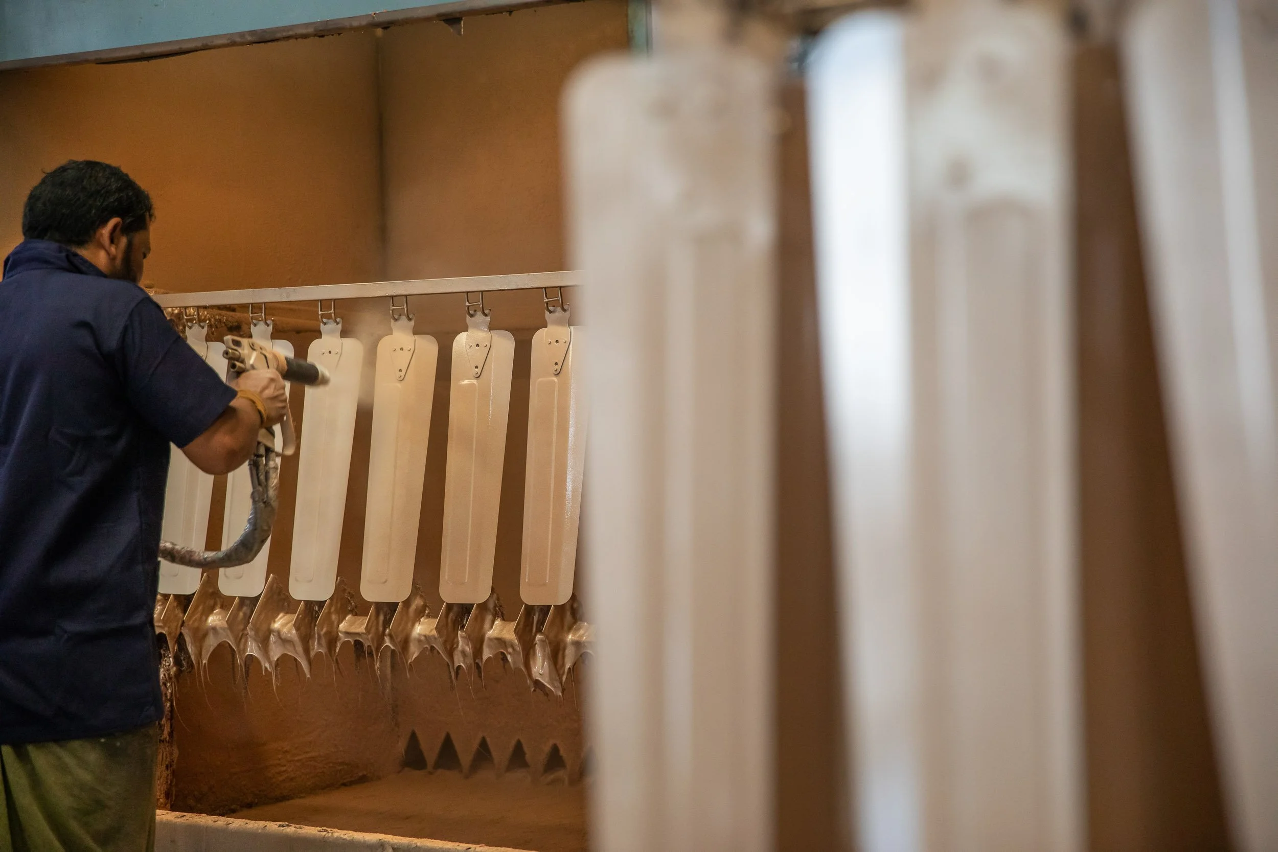 Interior industrial photography of a factory worker in a dark blue uniform inspecting vertically stacked rolls of material in a manufacturing facility.