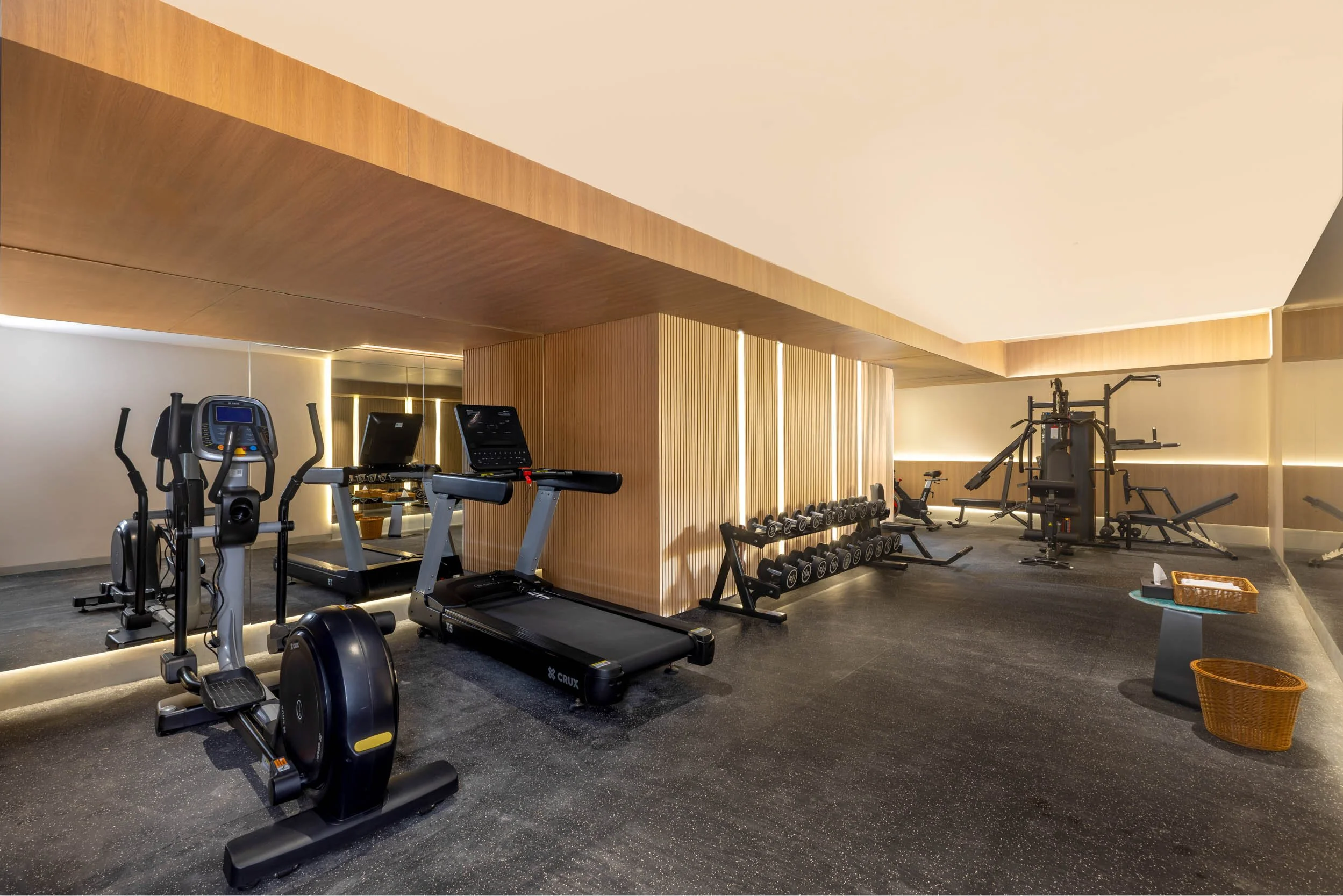 Interior photography of a modern hotel gym featuring treadmills, exercise equipment, large wall mirrors, and warm ambient lighting