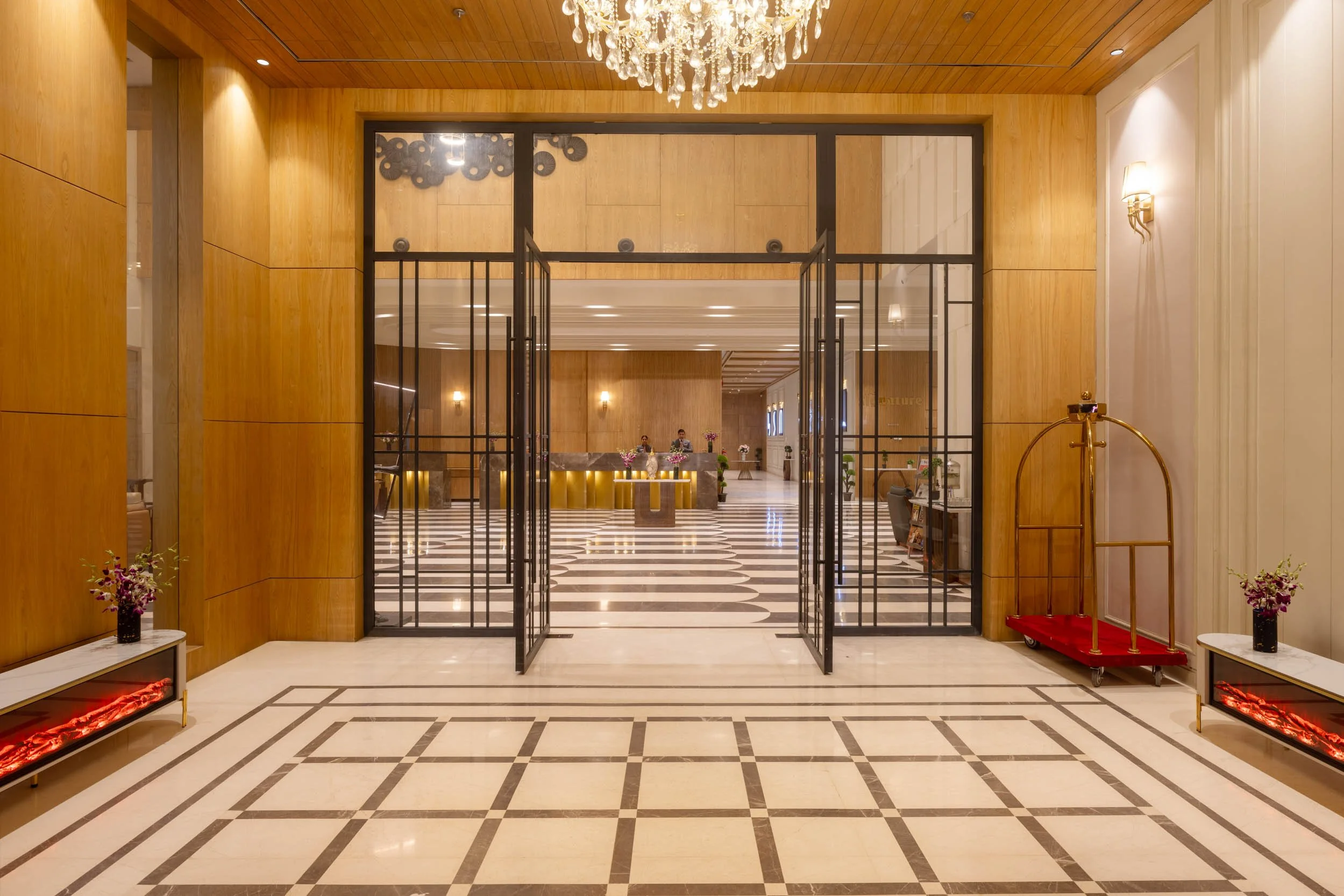 Interior photography of a luxury hotel entryway featuring glass double doors, a geometric patterned floor, wood-paneled walls, and warm chandelier lighting