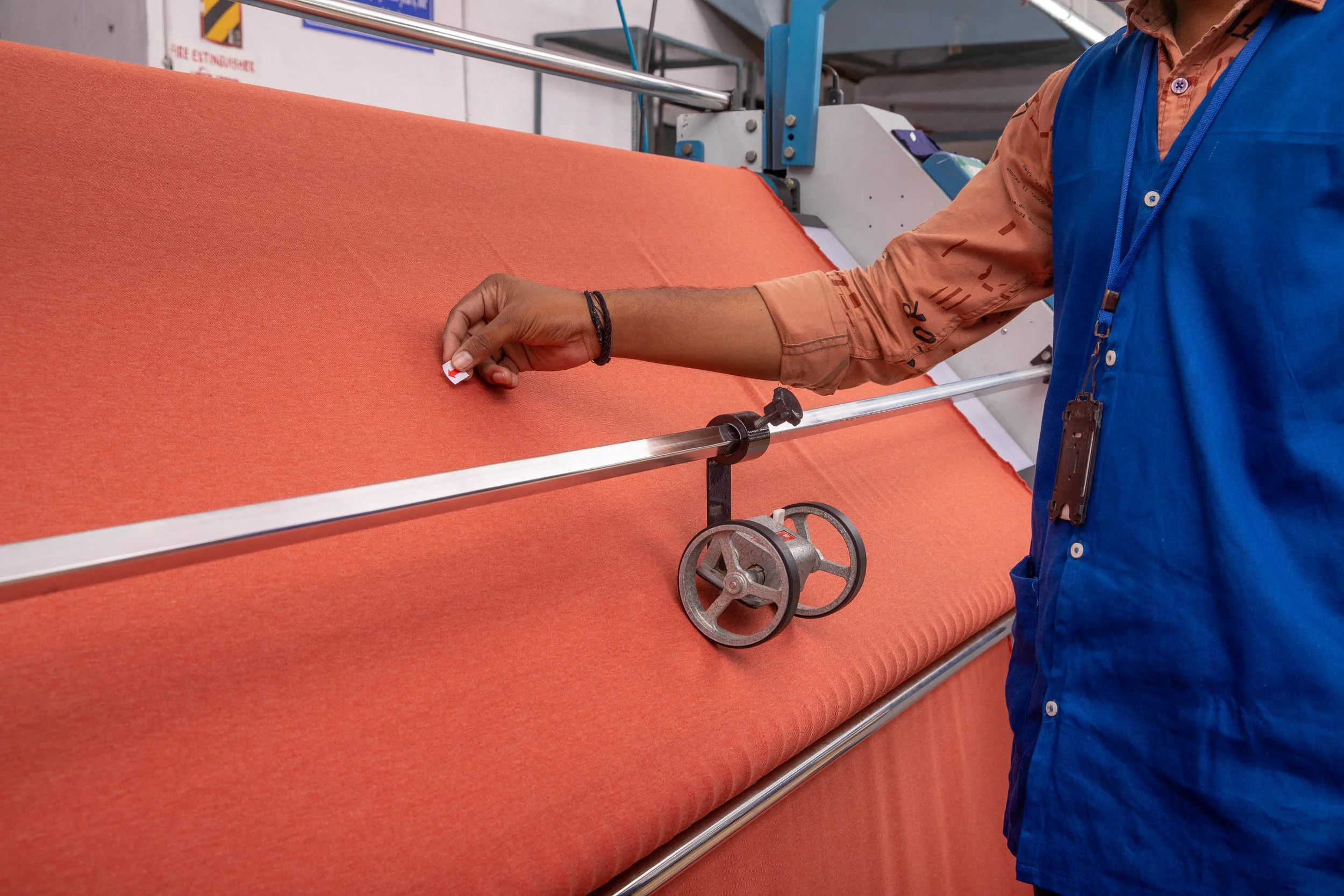 lose-up industrial photography of a factory worker in a blue uniform operating a mechanical handwheel on a machine processing wide red material.