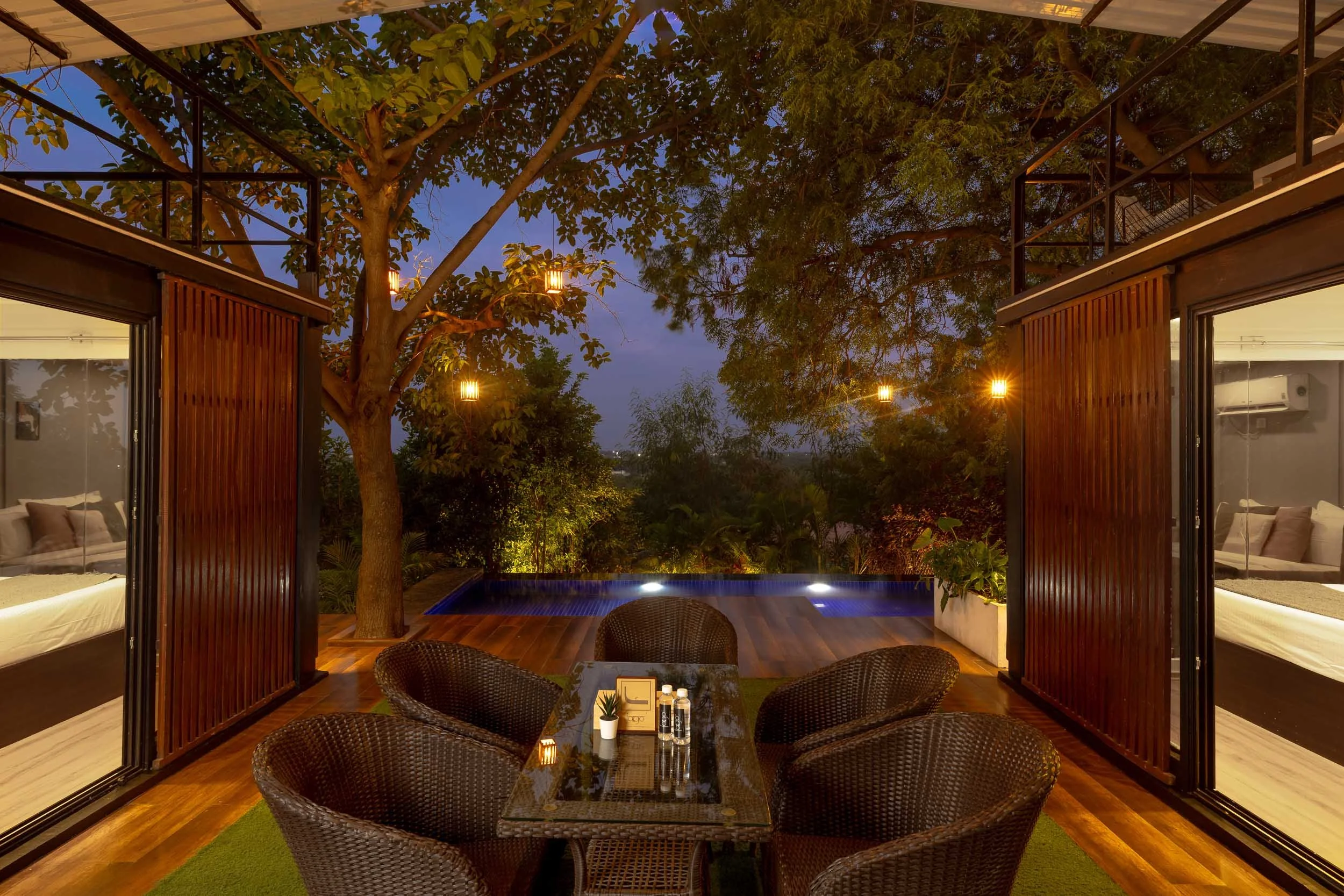 Exterior nighttime photography of a luxury staycation in Hyderabad, featuring an active outdoor fire pit surrounded by seating and trees