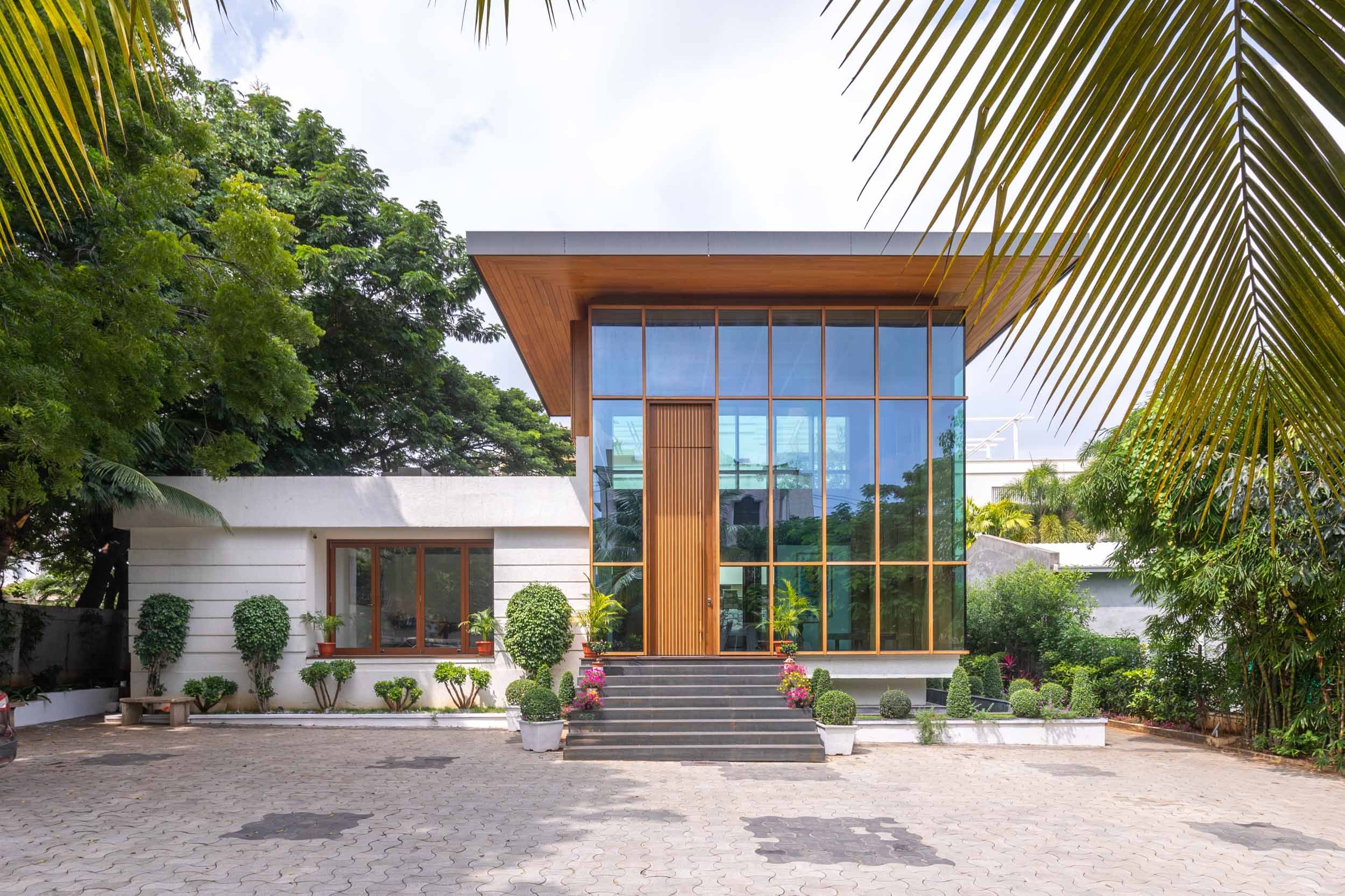 Professional exterior architectural photography of a modern, glass-fronted building, beautifully framed by lush tropical landscaping and a paved entrance