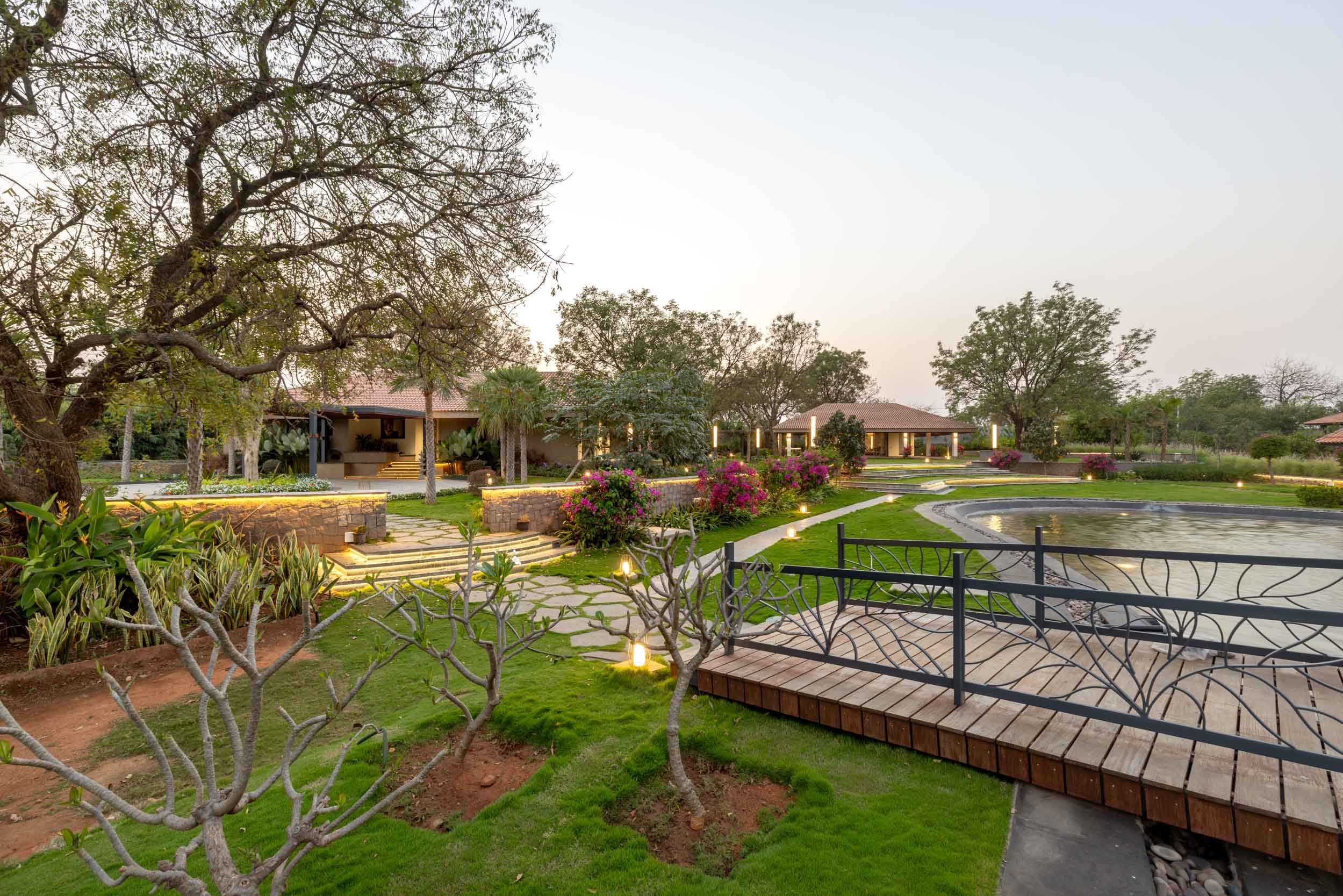 Expansive resort landscape design featuring a wooden footbridge over a scenic water feature, surrounded by manicured lawns and mature trees