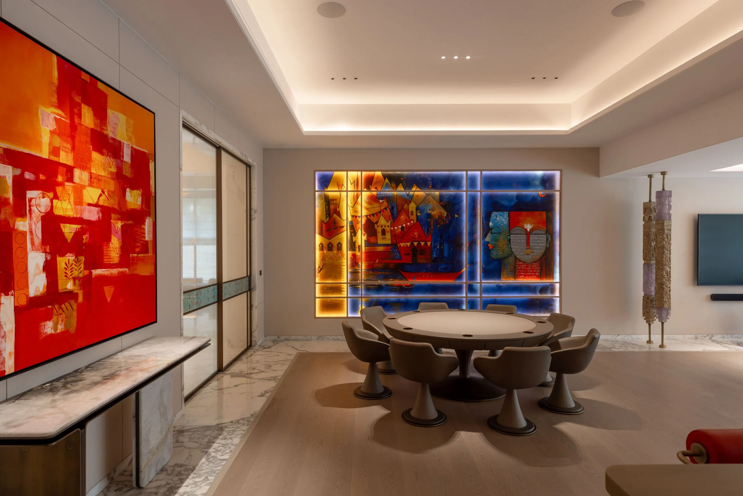 Modern open-plan dining area featuring a round table, warm architectural ceiling lighting, and two large, vibrant abstract paintings