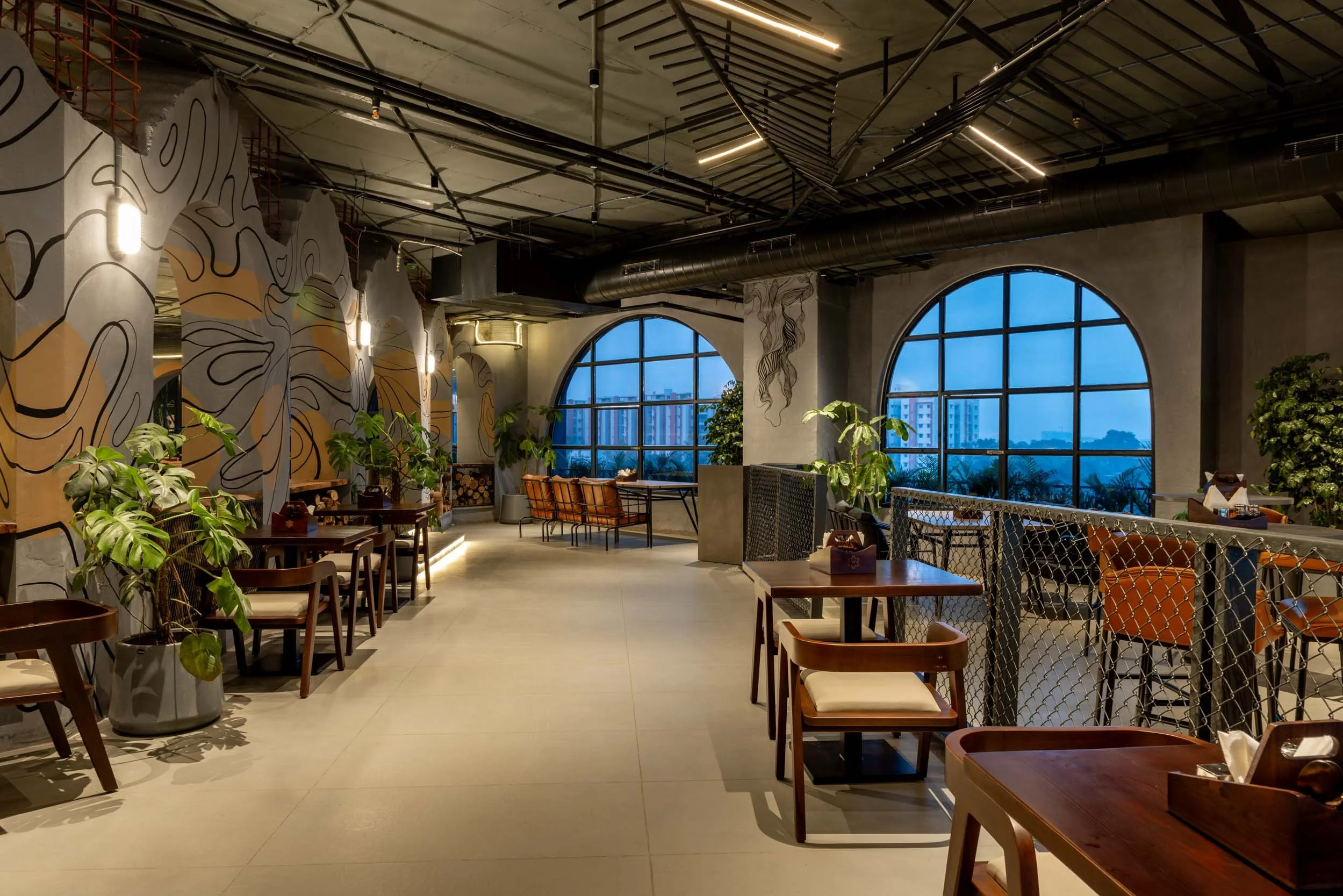 Commercial interior photography showcasing a spacious industrial-chic restaurant, highlighting exposed ceiling architecture, arched window design, and modern rustic hospitality interiors