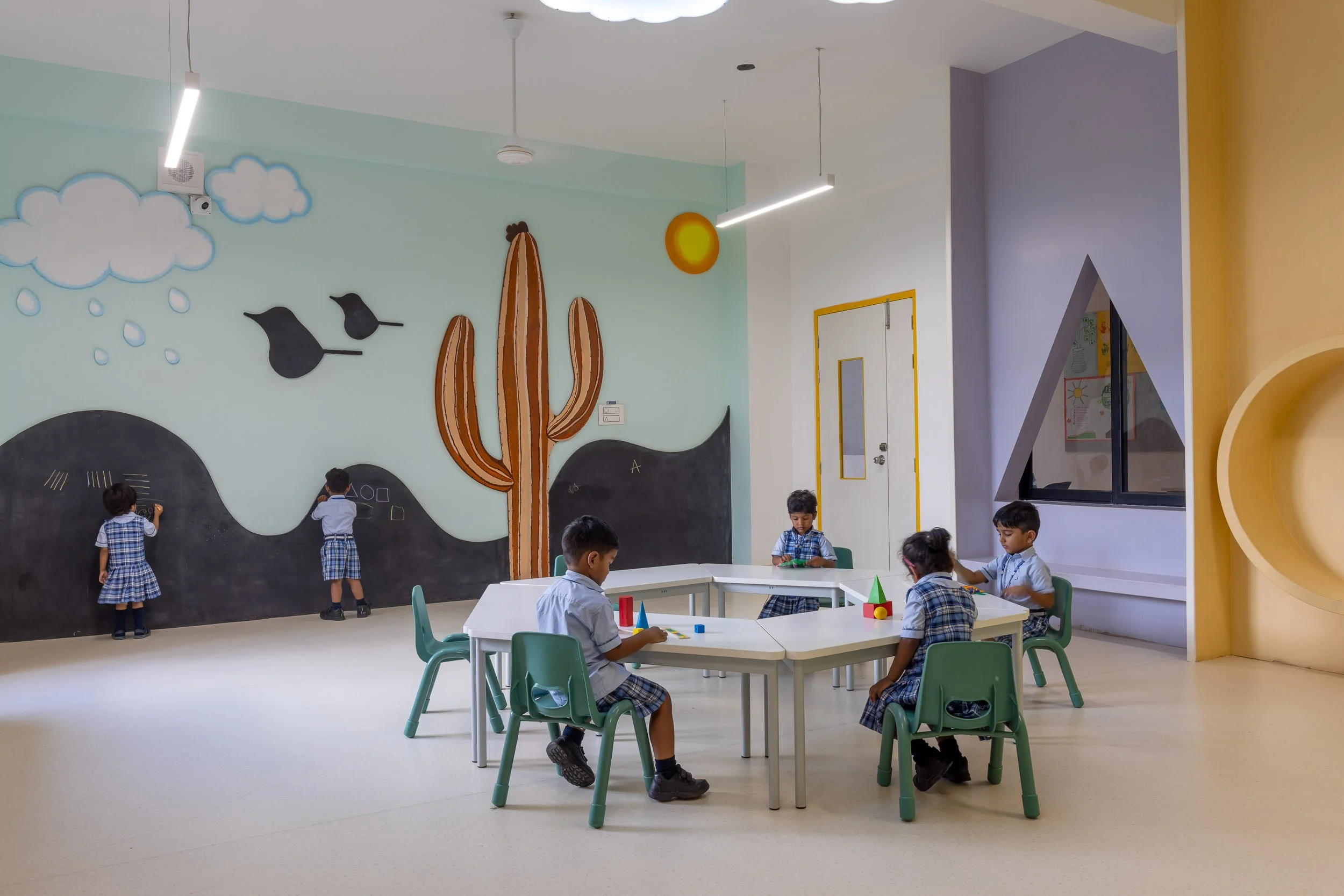 Interior school photography of young students sitting at a table in a brightly colored early learning classroom with a playful wall mural