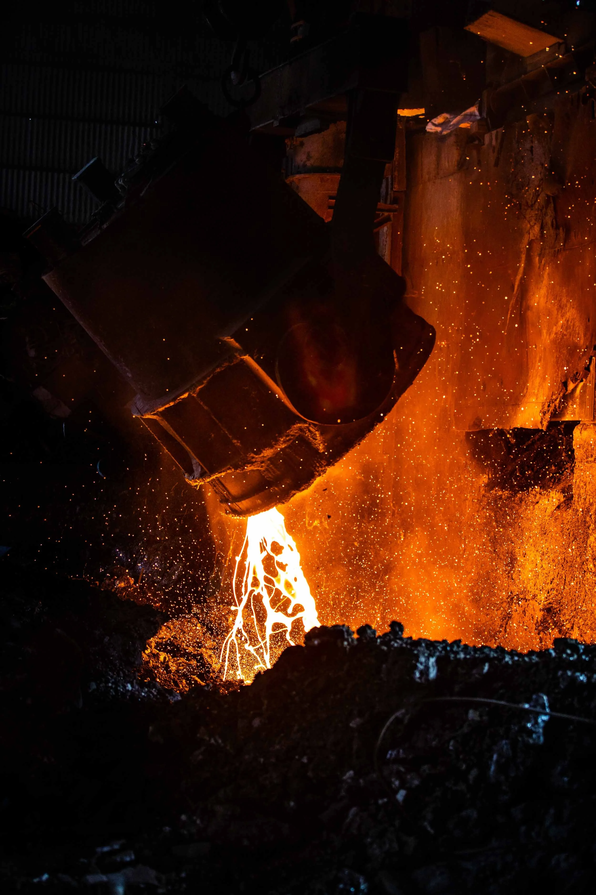 Dramatic industrial photography of glowing molten metal being poured in a heavy manufacturing foundry.