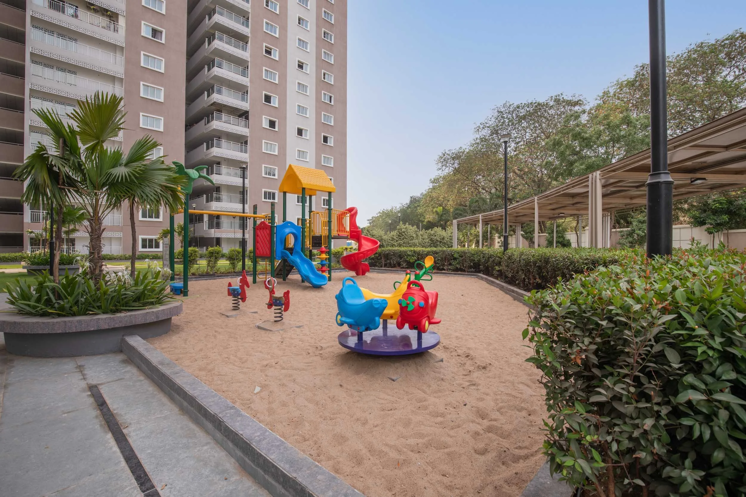 Residential real estate photography highlighting family-friendly outdoor amenities, featuring a colorful playground surrounded by lush landscaping and modern apartments