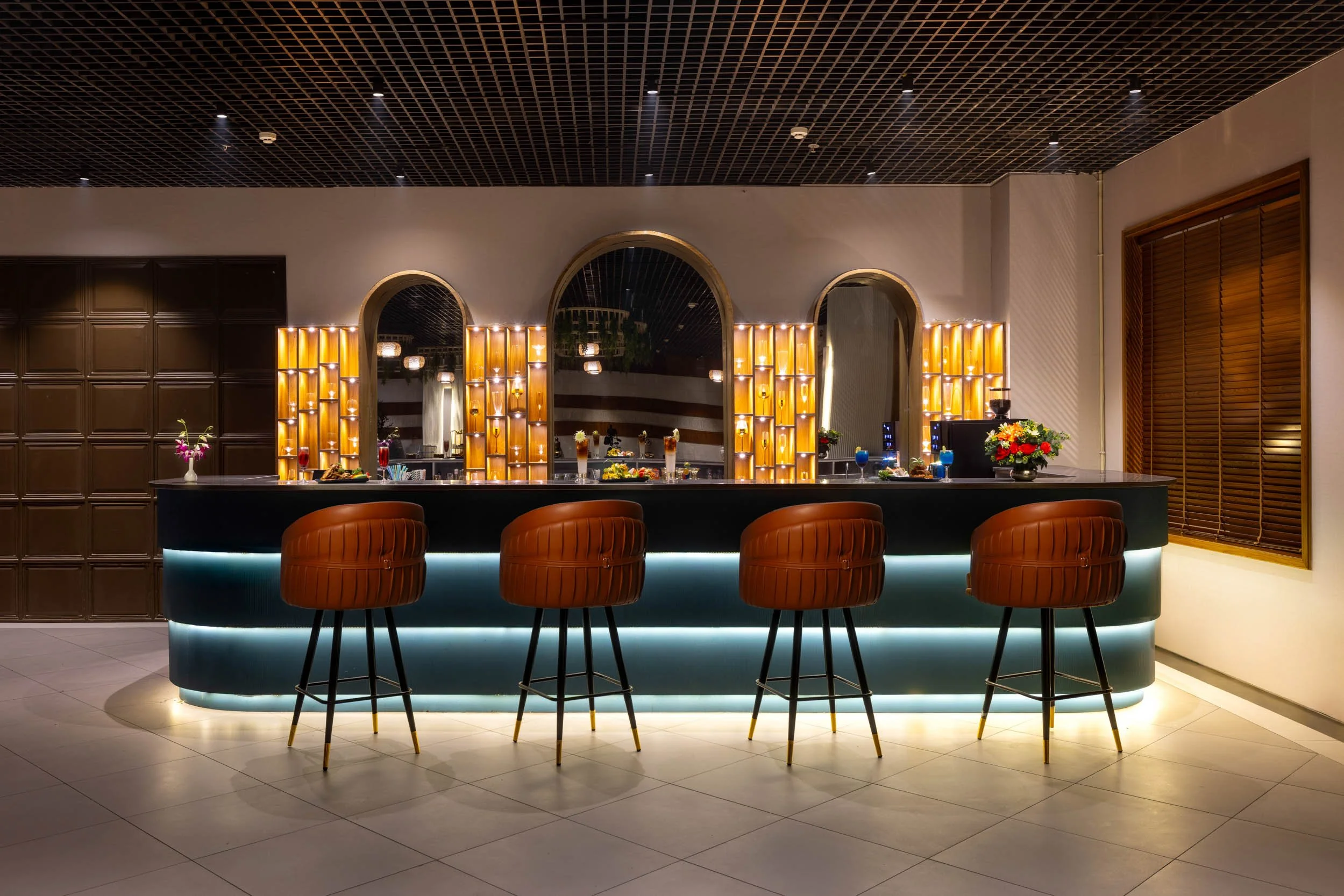 Interior photography of a luxury hotel bar featuring an illuminated counter, leather bar stools, arched shelving displays, and warm ambient lighting