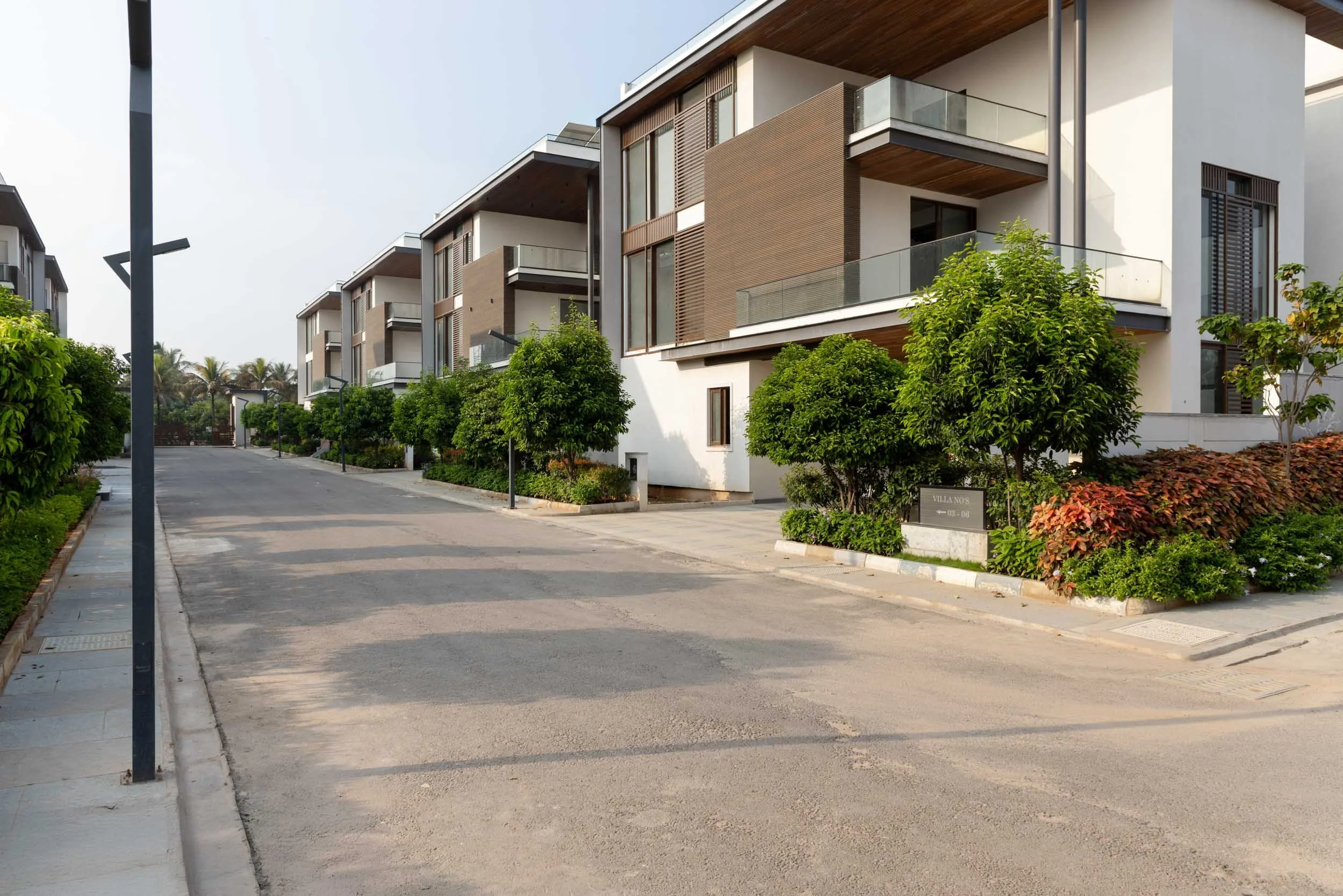 Residential real estate exterior photography showcasing a peaceful neighborhood street lined with modern luxury villas and paved driveways