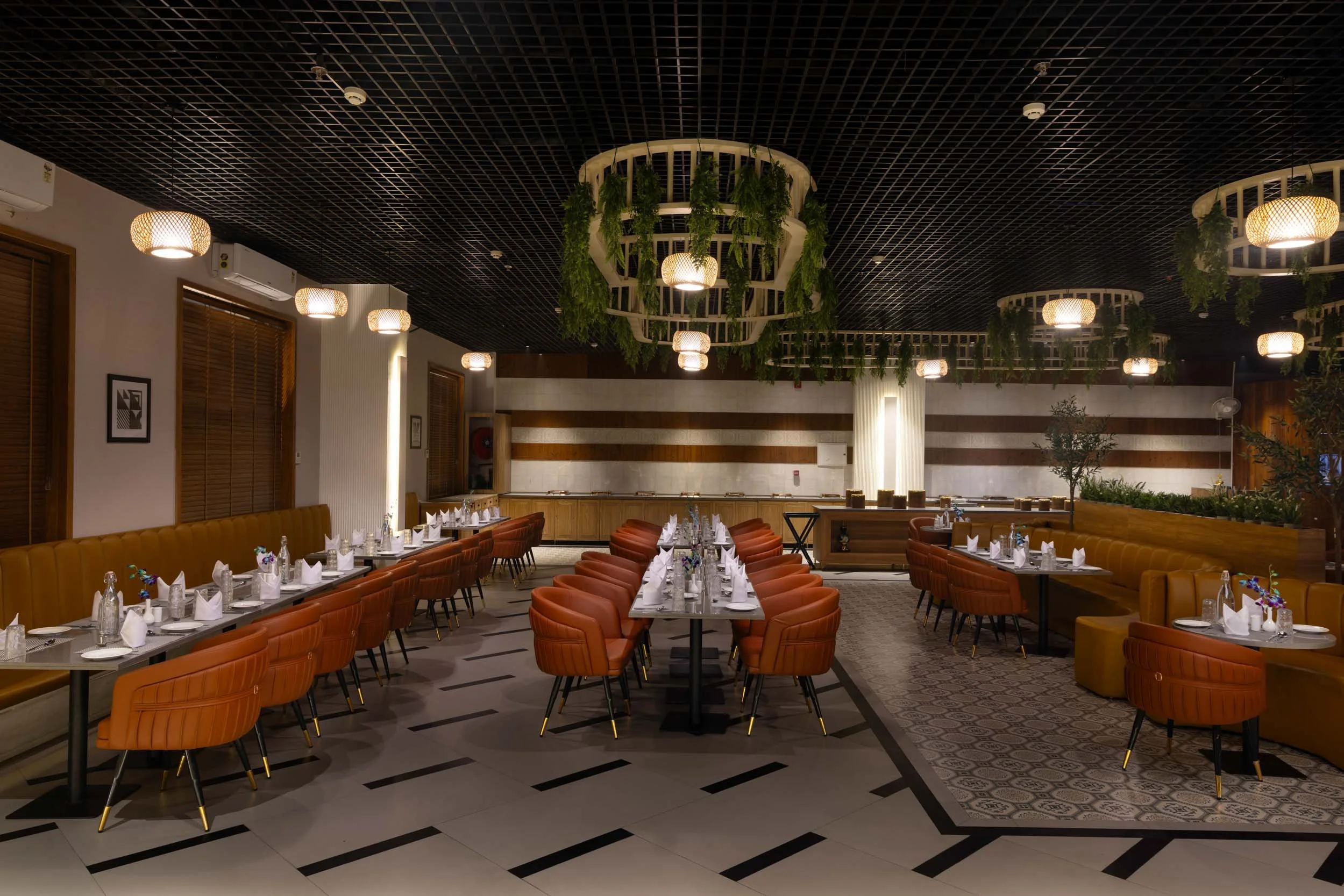 nterior photography of a luxury hotel restaurant featuring long dining tables, orange upholstered chairs, geometric flooring, and large circular ceiling lights