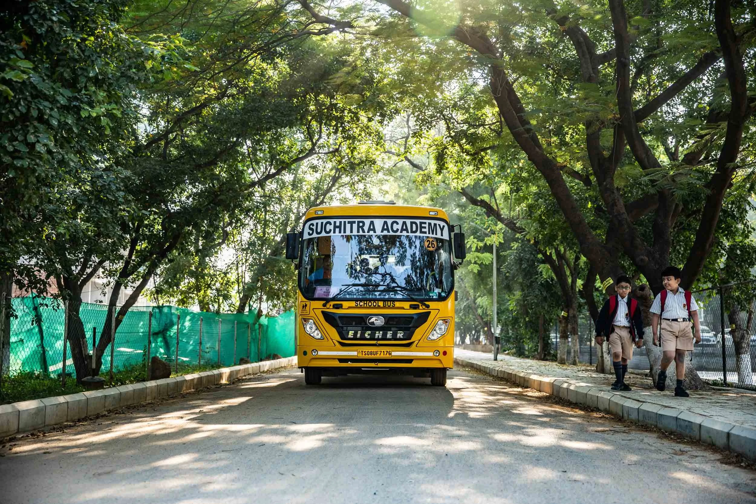 Exterior campus photography of a school bus arriving on a lush, tree-lined driveway at an educational institution | Ravi Varma Photography & Films