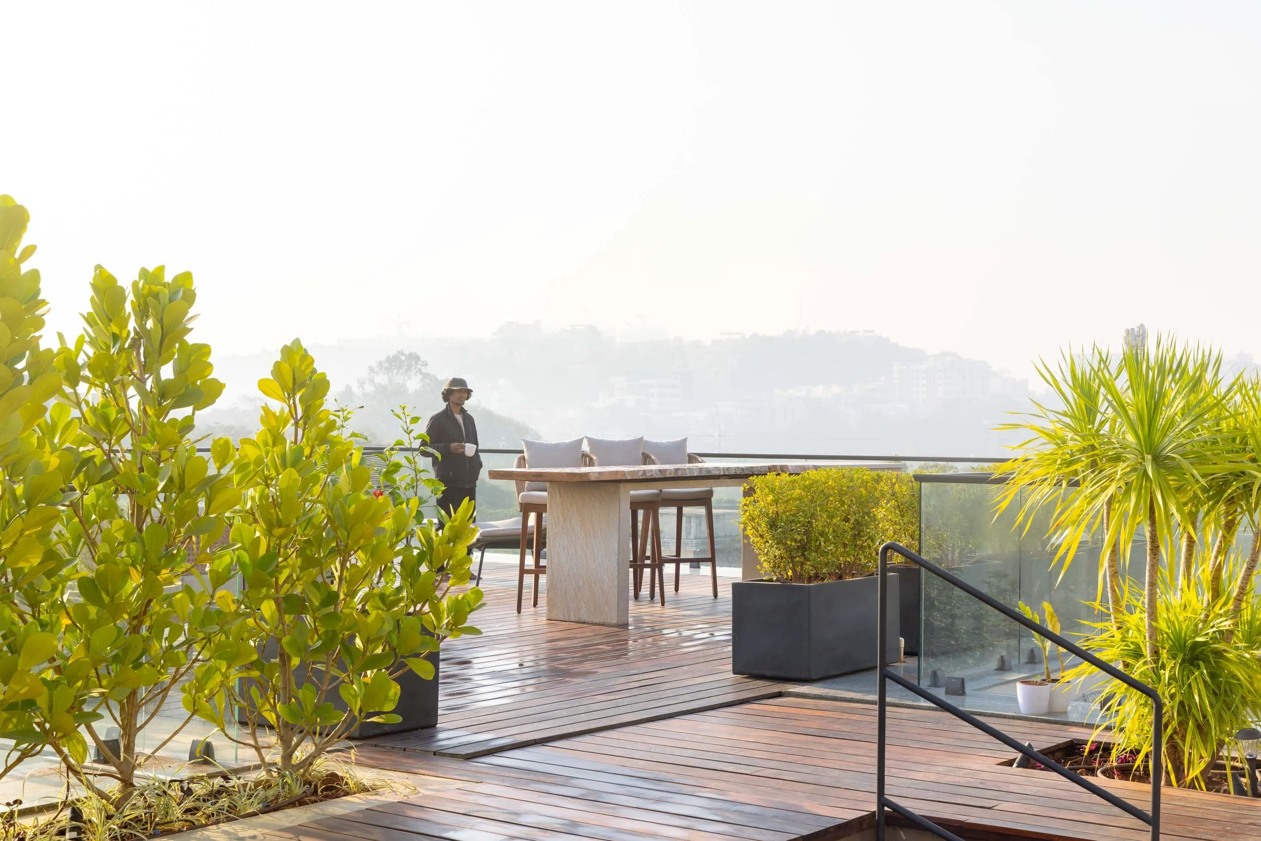 levated rooftop terrace featuring a wooden deck, minimalist railing, potted greenery, and a scenic view of distant hills