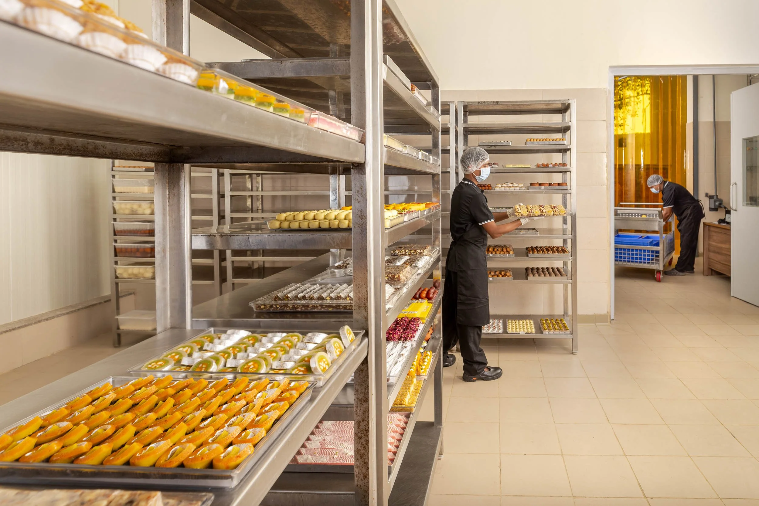 Interior industrial photography of a worker managing large racks of baked goods in a commercial bakery and food processing facility