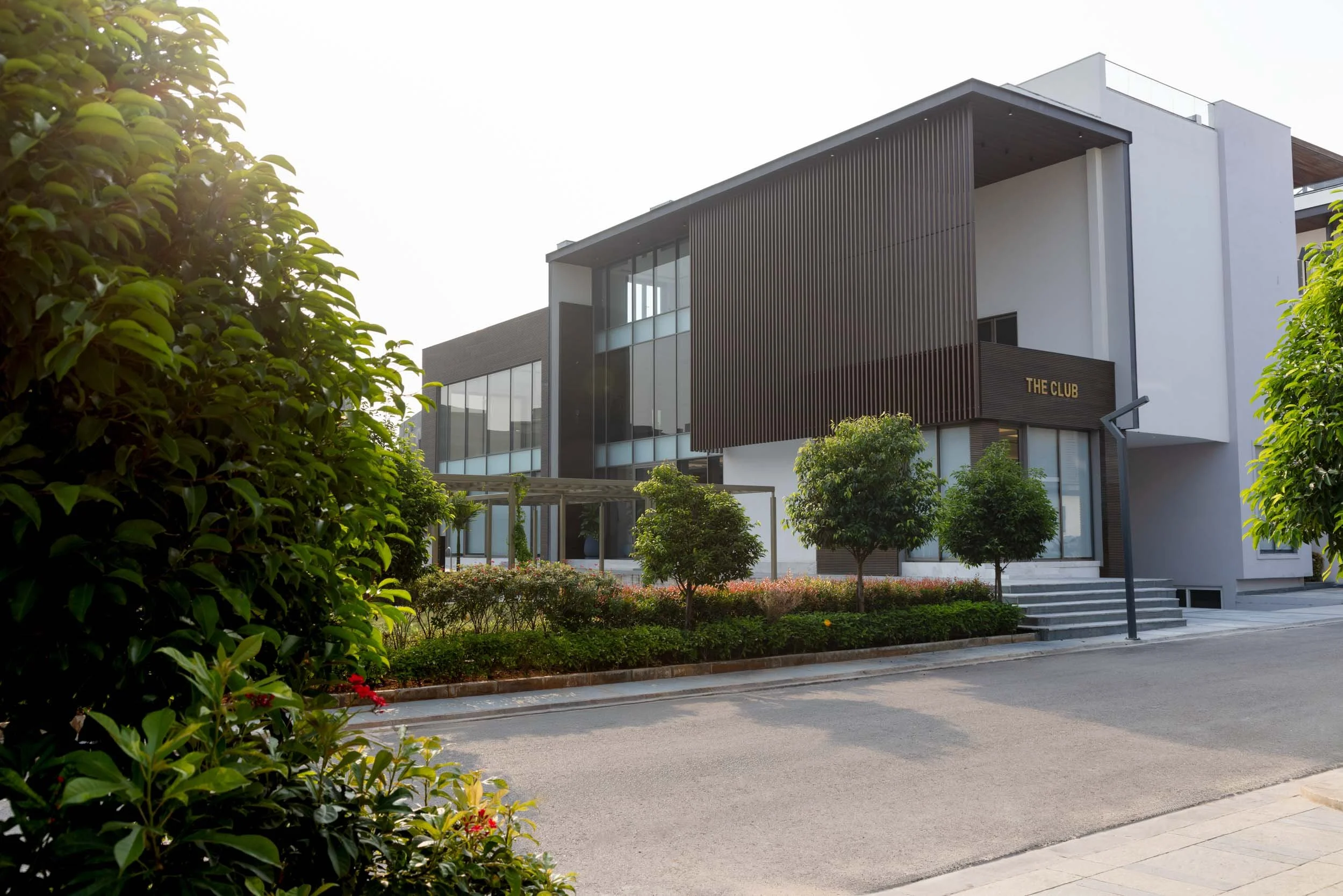 Exterior real estate photography showcasing a contemporary modern home with unique architectural screening, an expansive driveway, and manicured landscaping