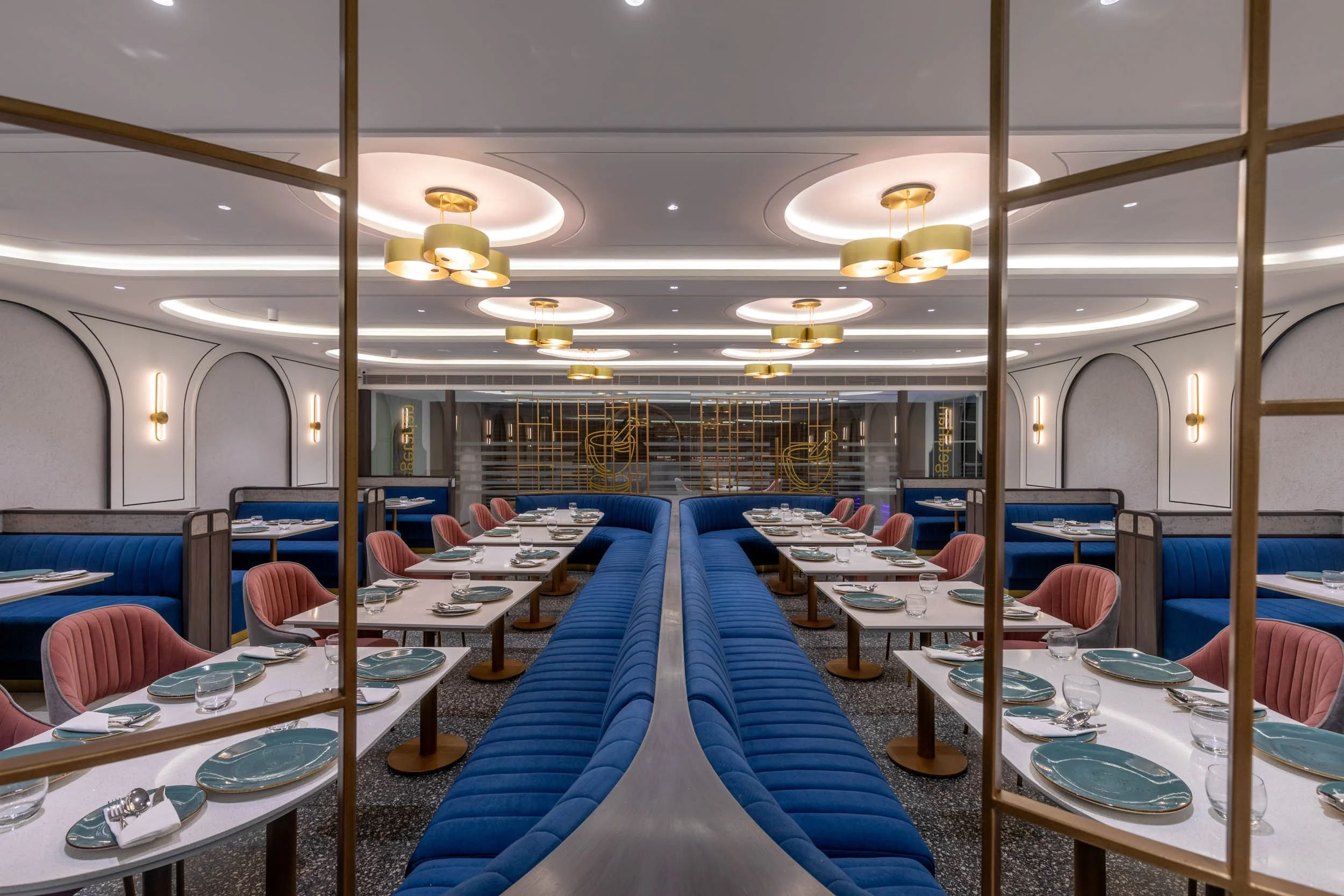Commercial interior photography showcasing a luxury hospitality dining area, highlighting reflective architectural elements, custom blue booth seating, and elegant restaurant interior design
