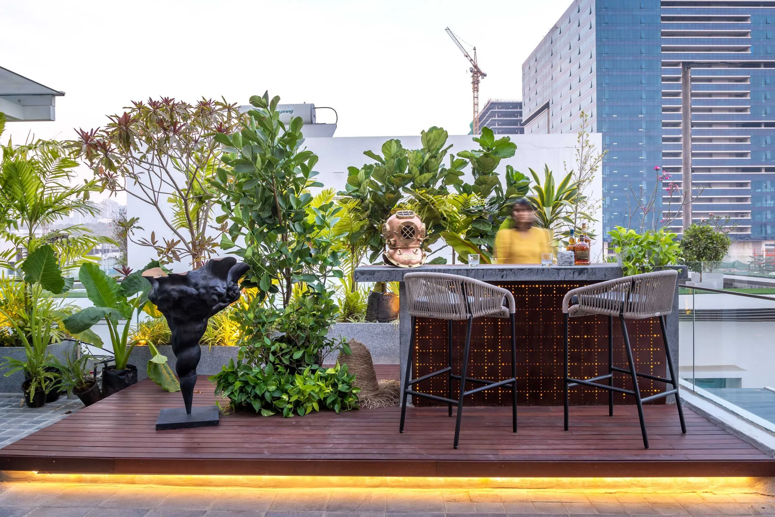 Rooftop terrace design featuring an elevated wooden deck with integrated LED lighting, outdoor dining furniture, potted greenery, and a city skyline backdrop