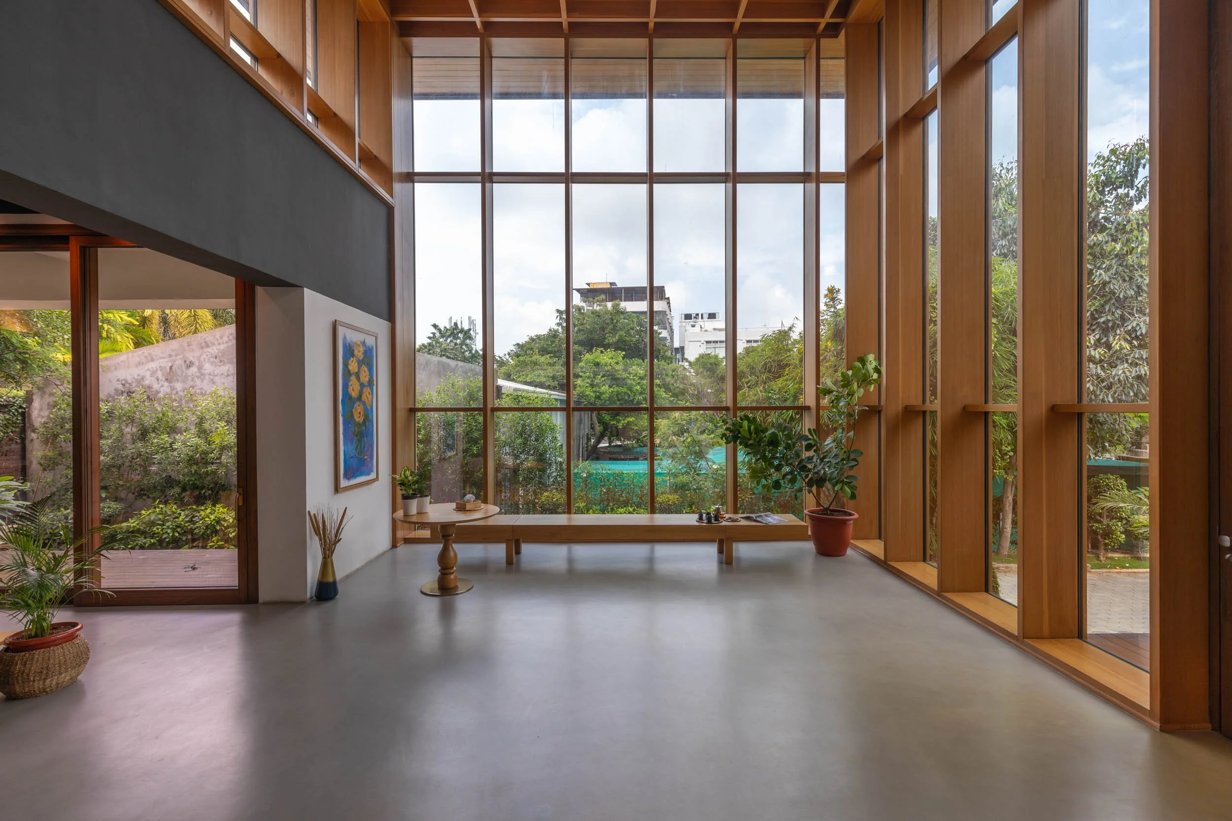 Professional interior architecture photography of a bright modern commercial space, highlighting warm wood slatted walls, polished floors, and expansive windows framing lush outdoor greenery