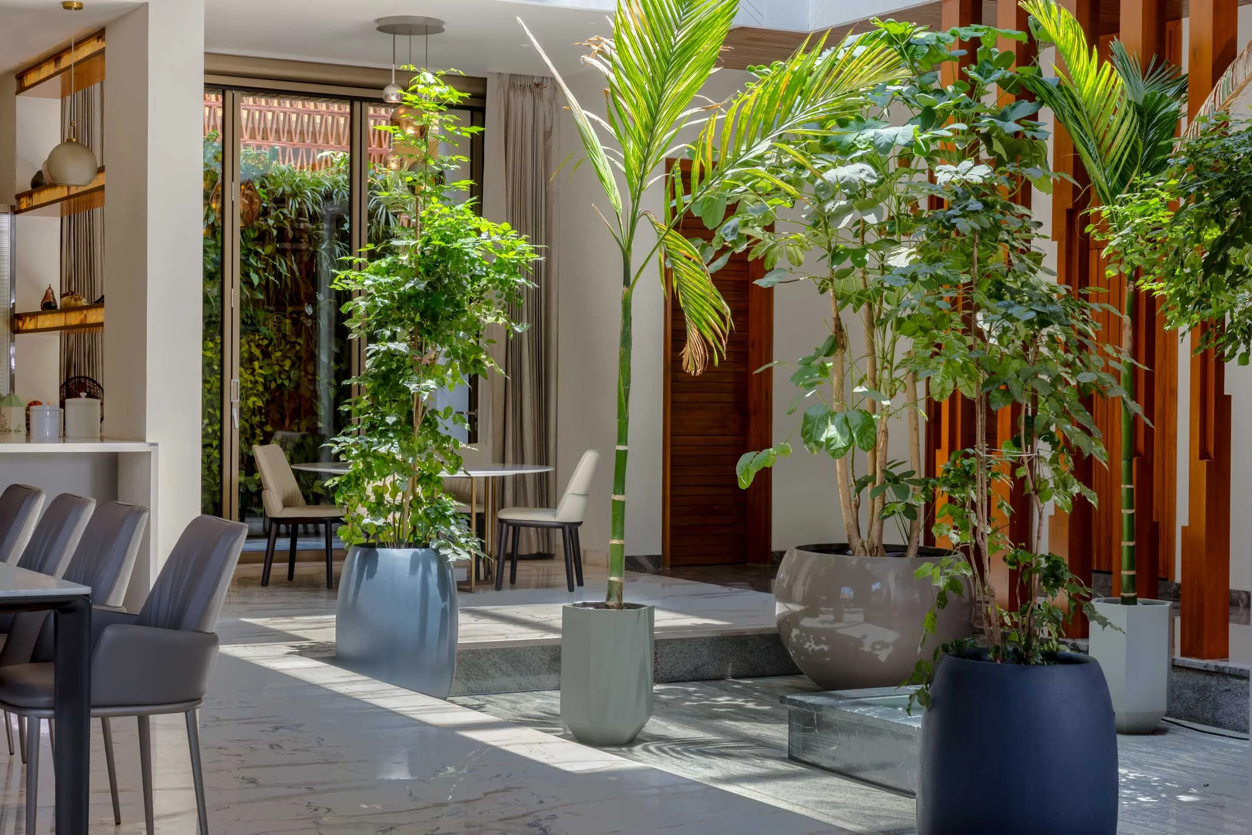Professional architectural photography of a serene residential outdoor living space, highlighting a shaded patio dining area, natural stone flooring, and lush potted greenery.