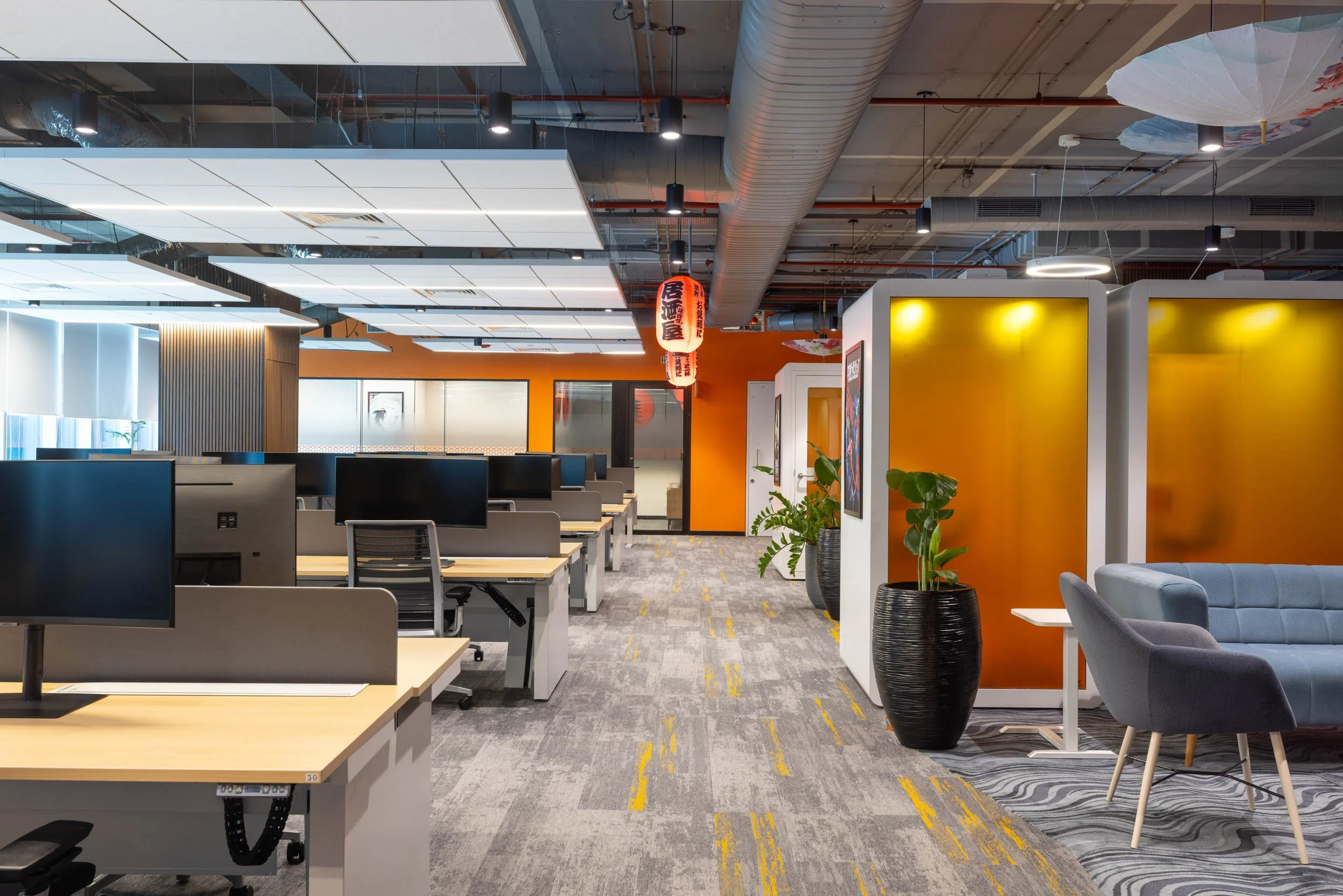Commercial interior photography showcasing a creative corporate workspace, highlighting open-plan desk arrangements, industrial ceiling design, and colorful breakout meeting pods