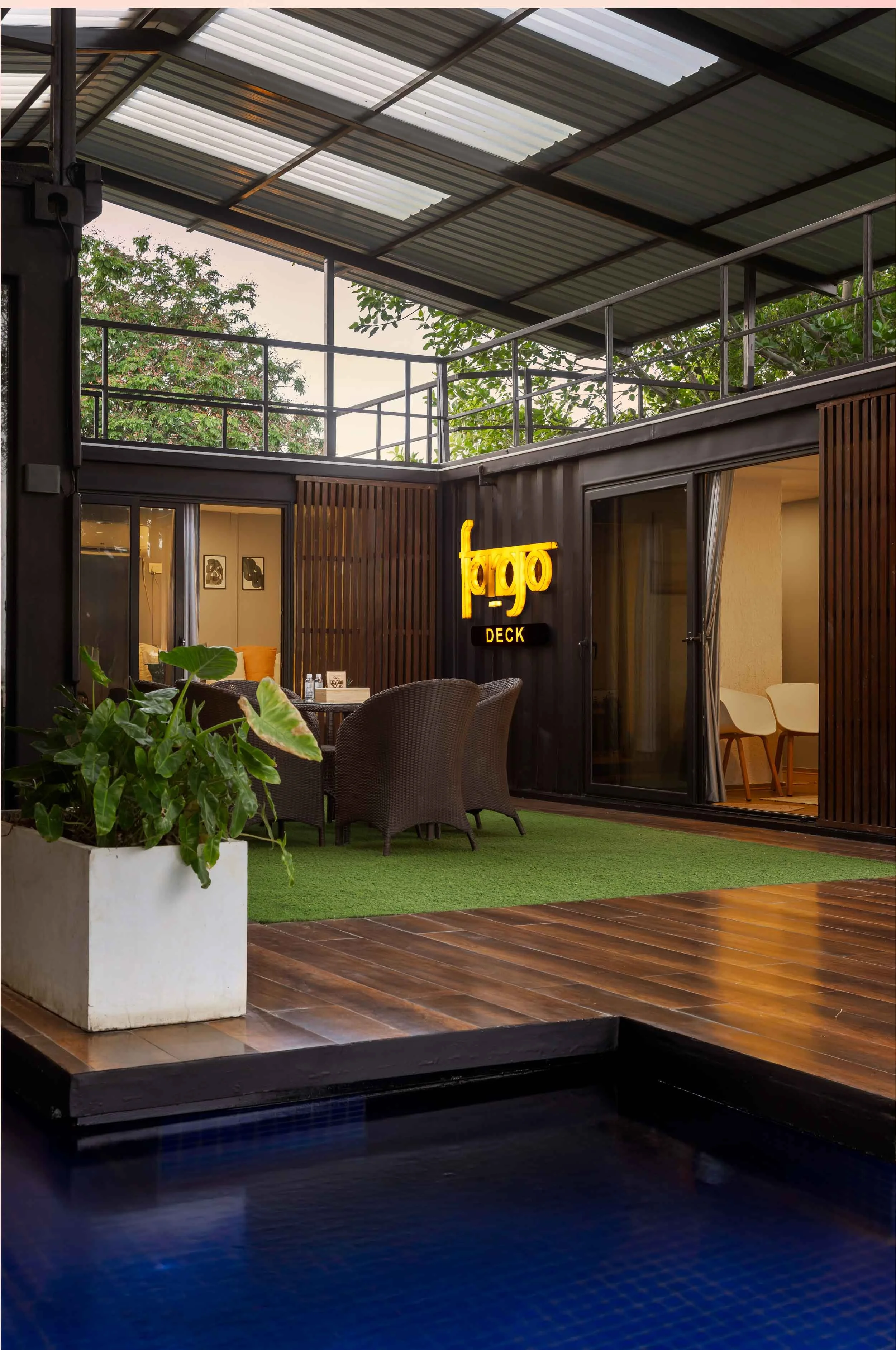 Interior daytime photography of a modern luxury staycation cabin in Hyderabad, looking out through large glass sliding doors toward a private wooden deck and plunge pool.