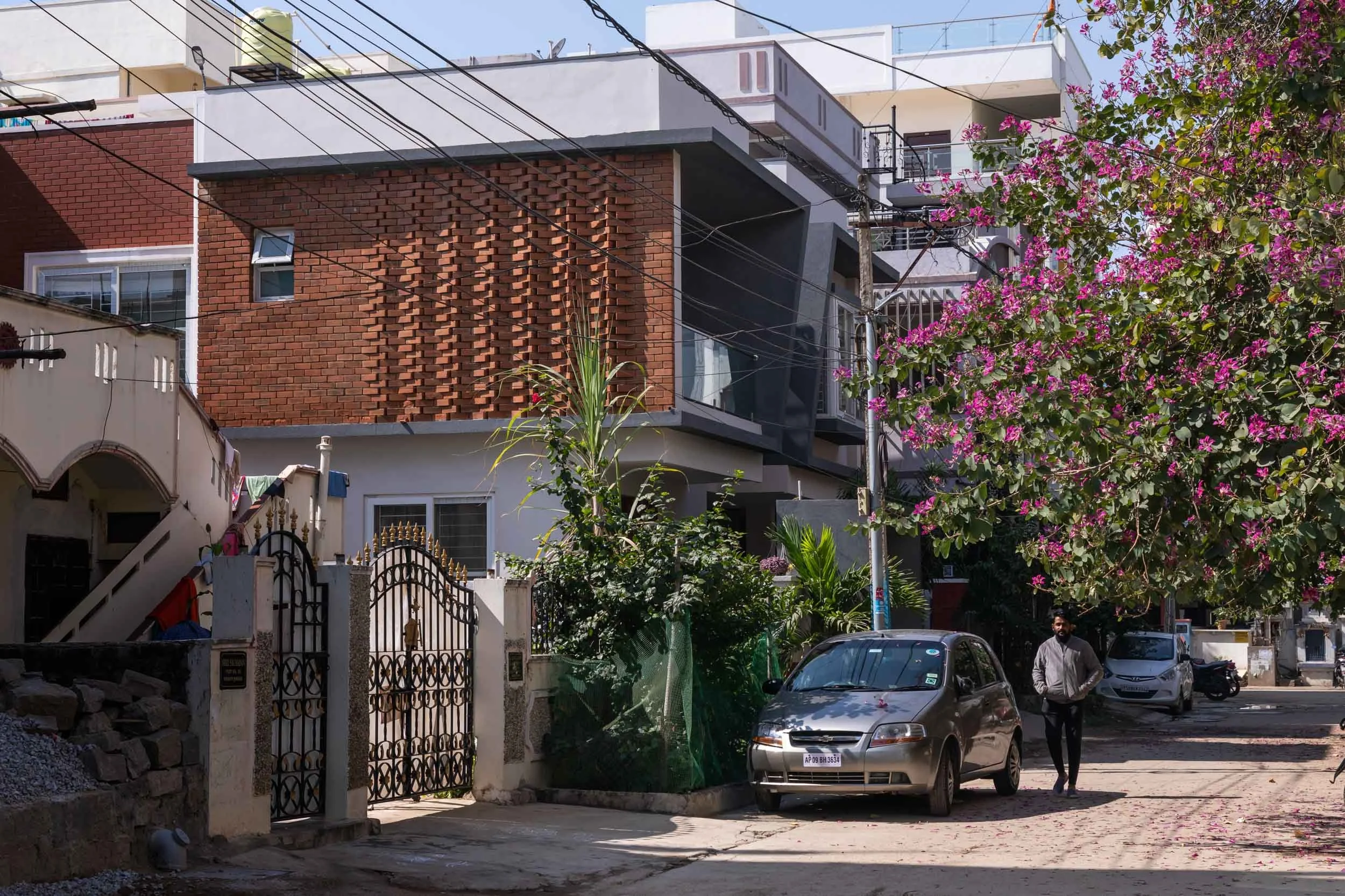Professional exterior architectural photography of a modern residential home, capturing a wide street-level view and highlighting a prominent perforated terracotta facade and neighborhood context