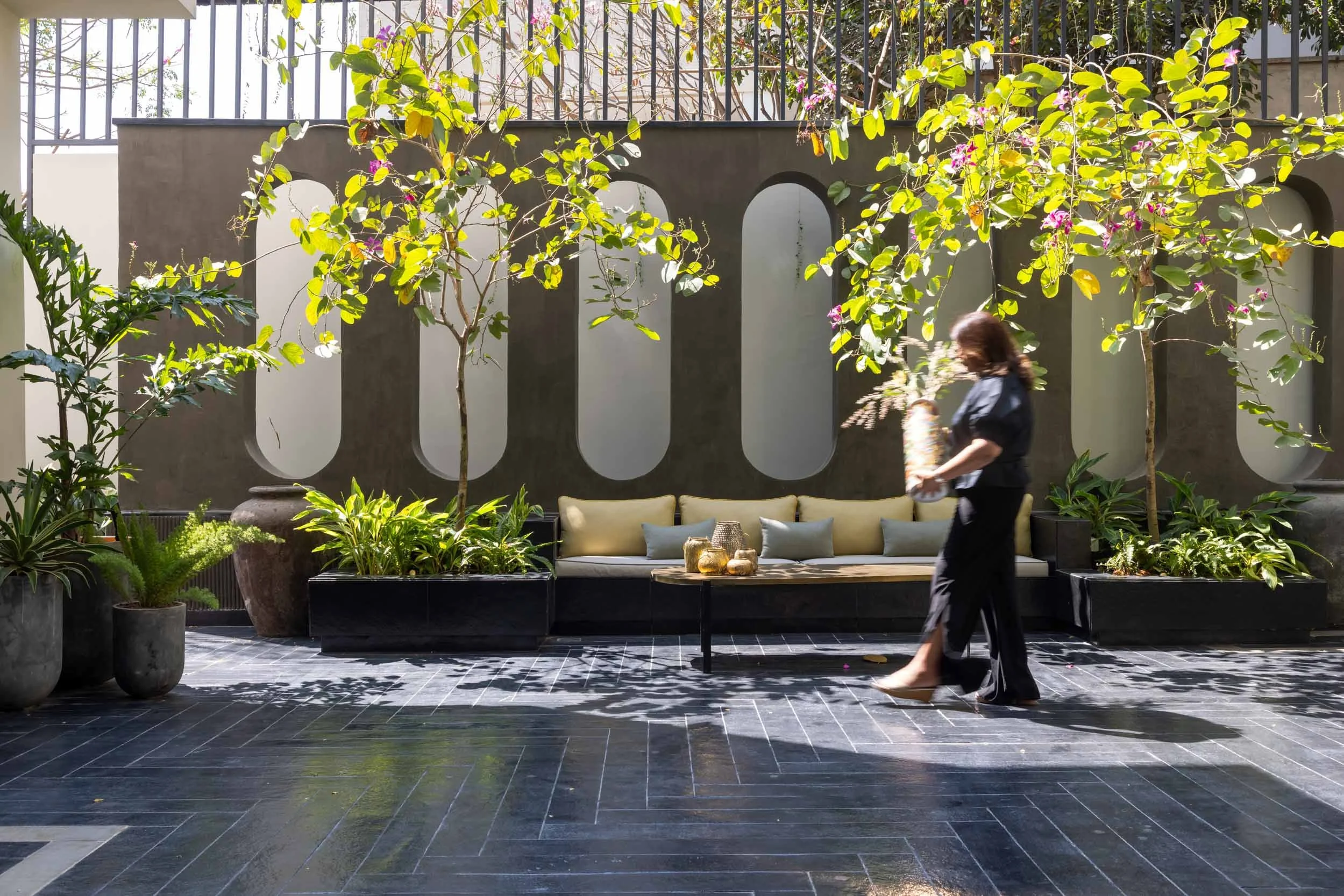 Modern landscape design featuring a dark reflective courtyard surface, vertical slatted fencing, and a sunlit tree canopy.
