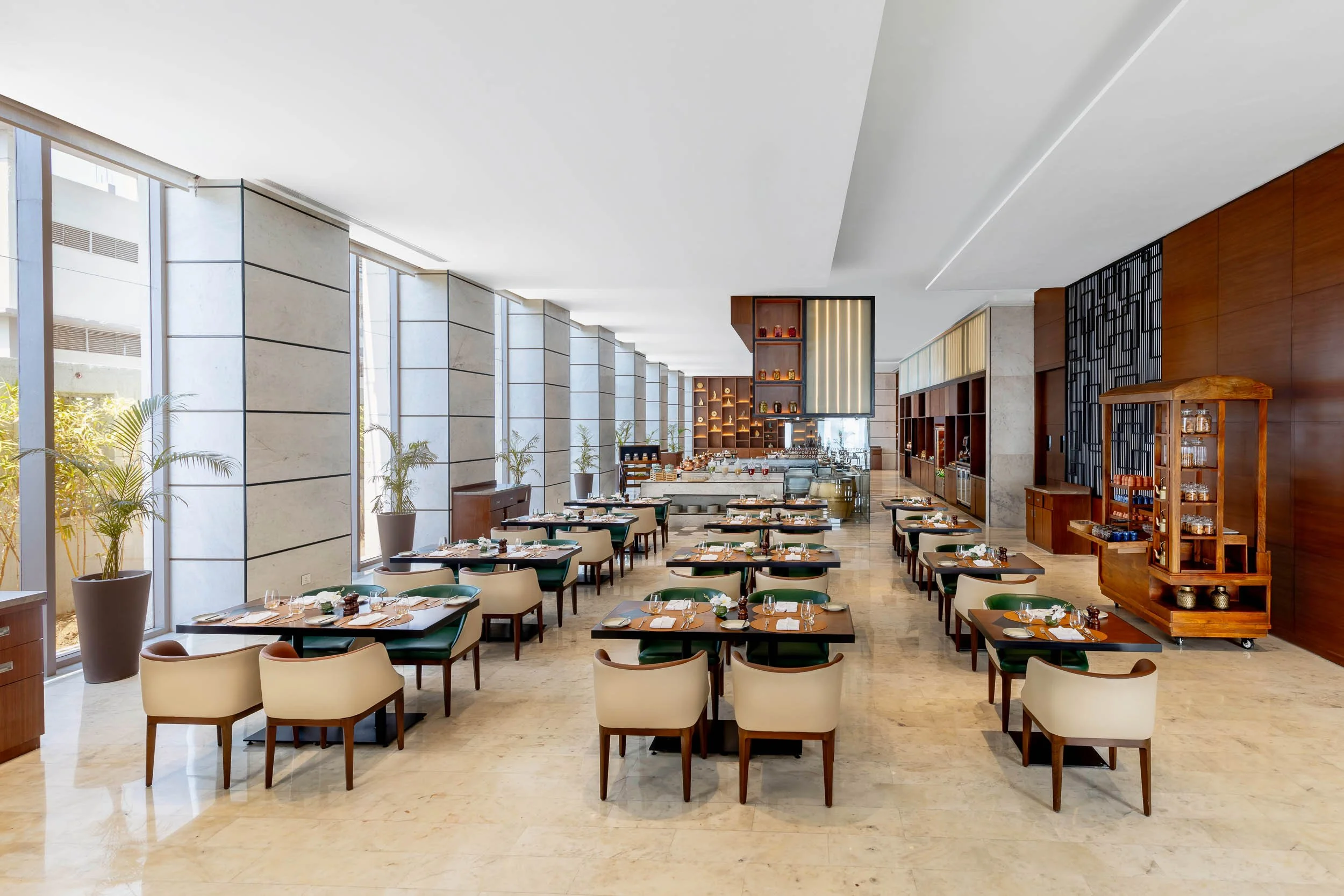 Interior photography of a long, bright hotel restaurant featuring rows of modern dining tables, large floor-to-ceiling windows, and patterned ceiling panels.