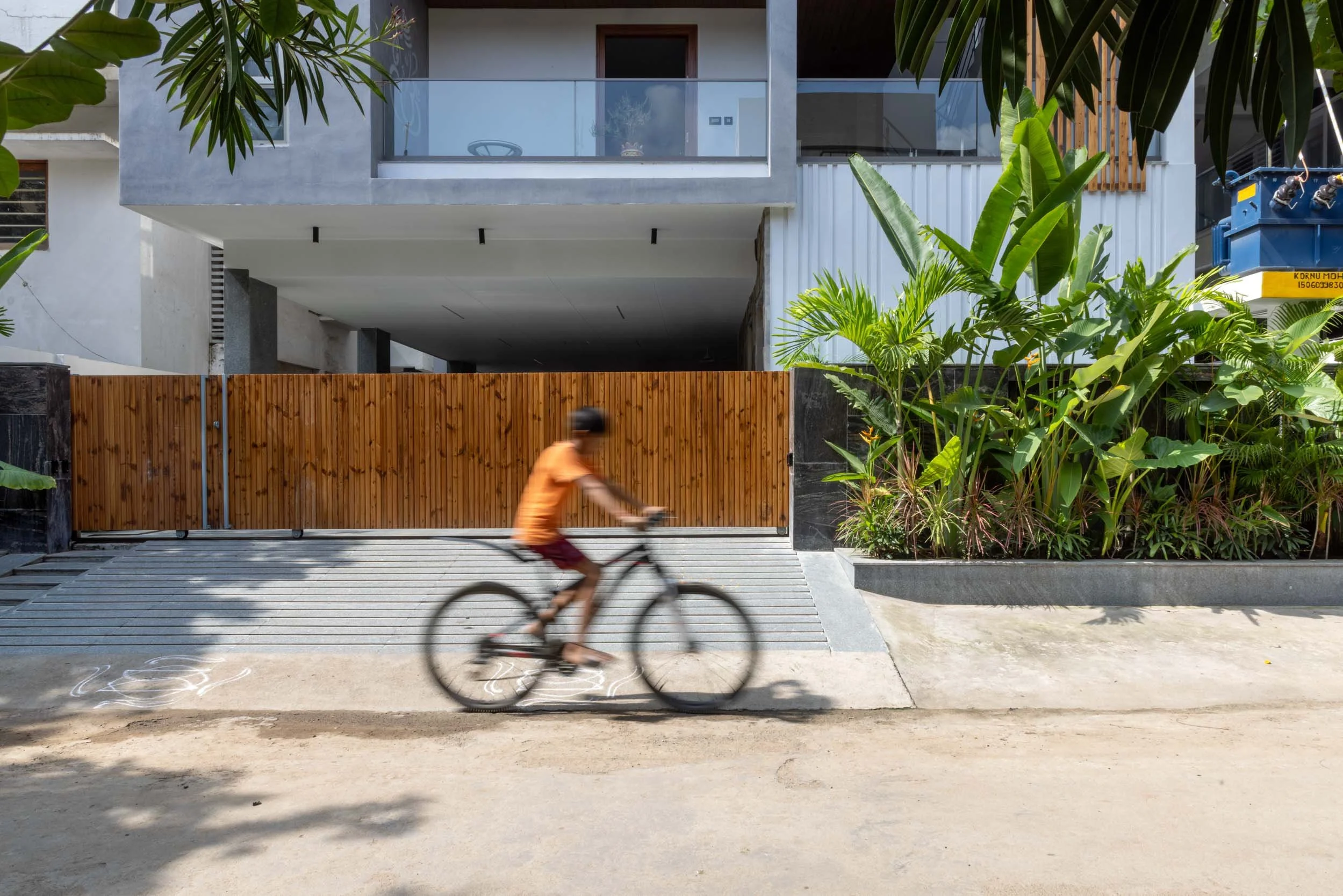 Professional exterior architectural photography of a modern residential home, capturing a vibrant street-level view with a child on a bicycle adding a perfect lifestyle element