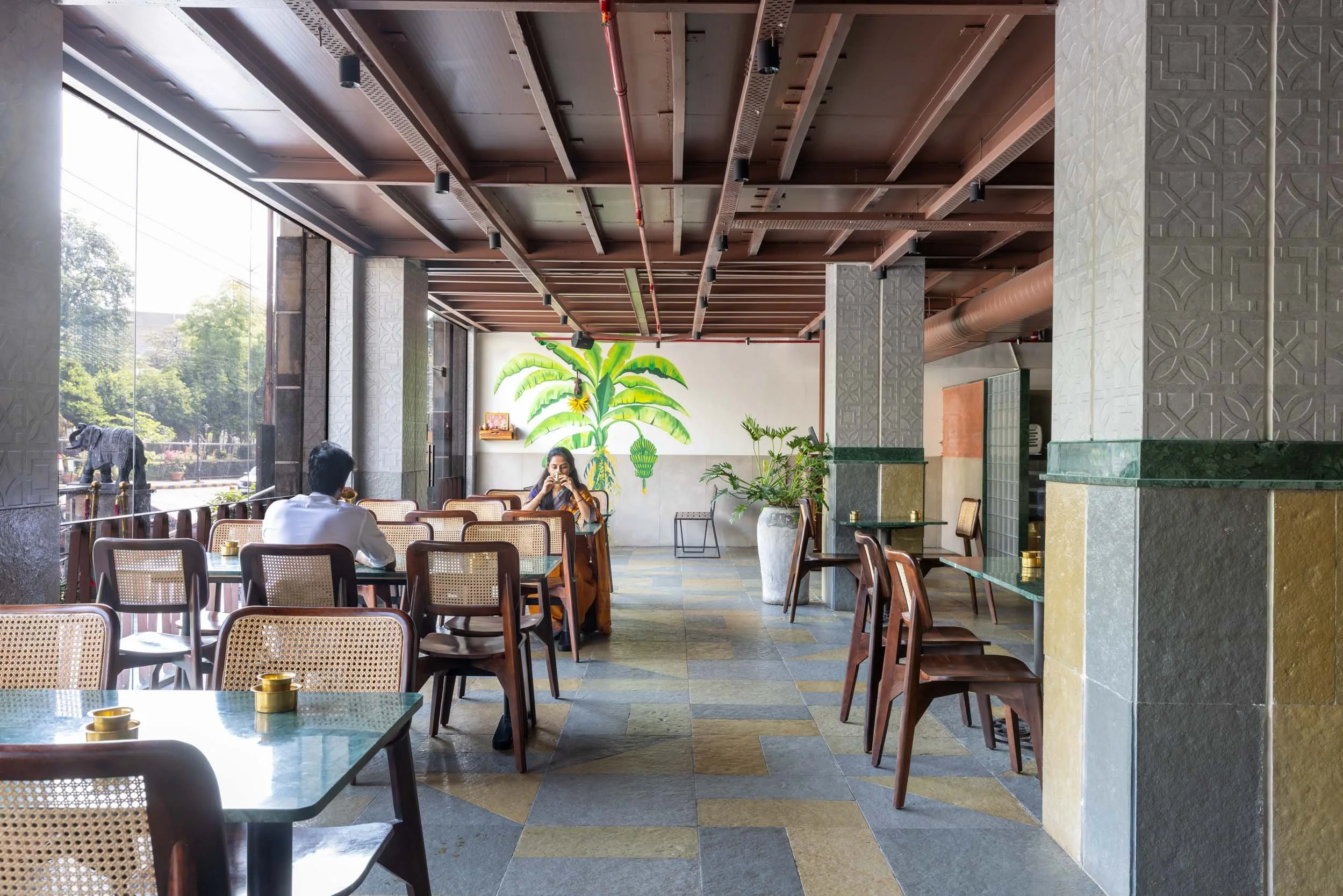Commercial interior photography showcasing a modern biophilic cafe design, highlighting indoor-outdoor dining spaces, custom wooden ceilings, and natural daylighting