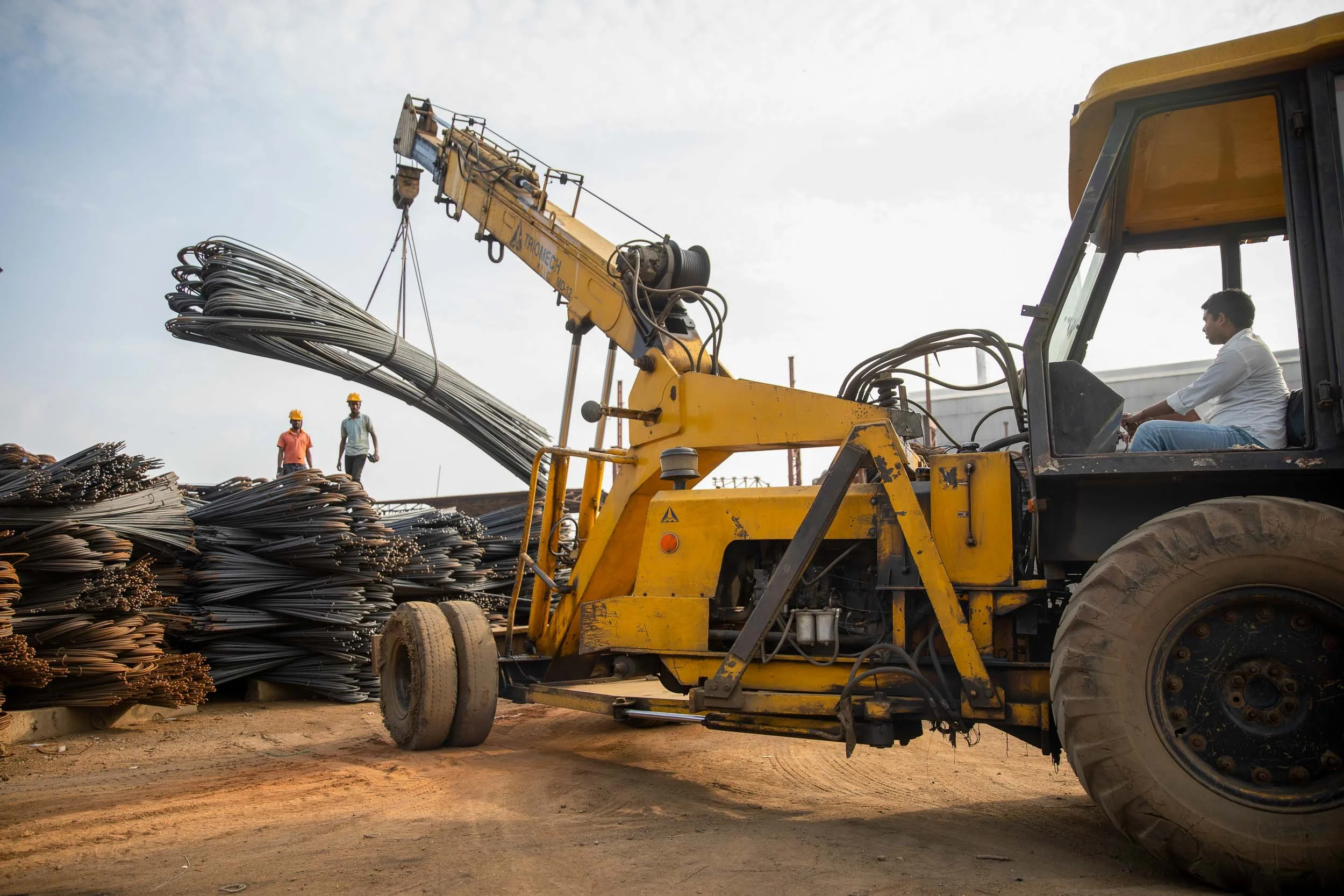 Exterior industrial photography of heavy machinery lifting a bundle of steel rebar at a construction and infrastructure site
