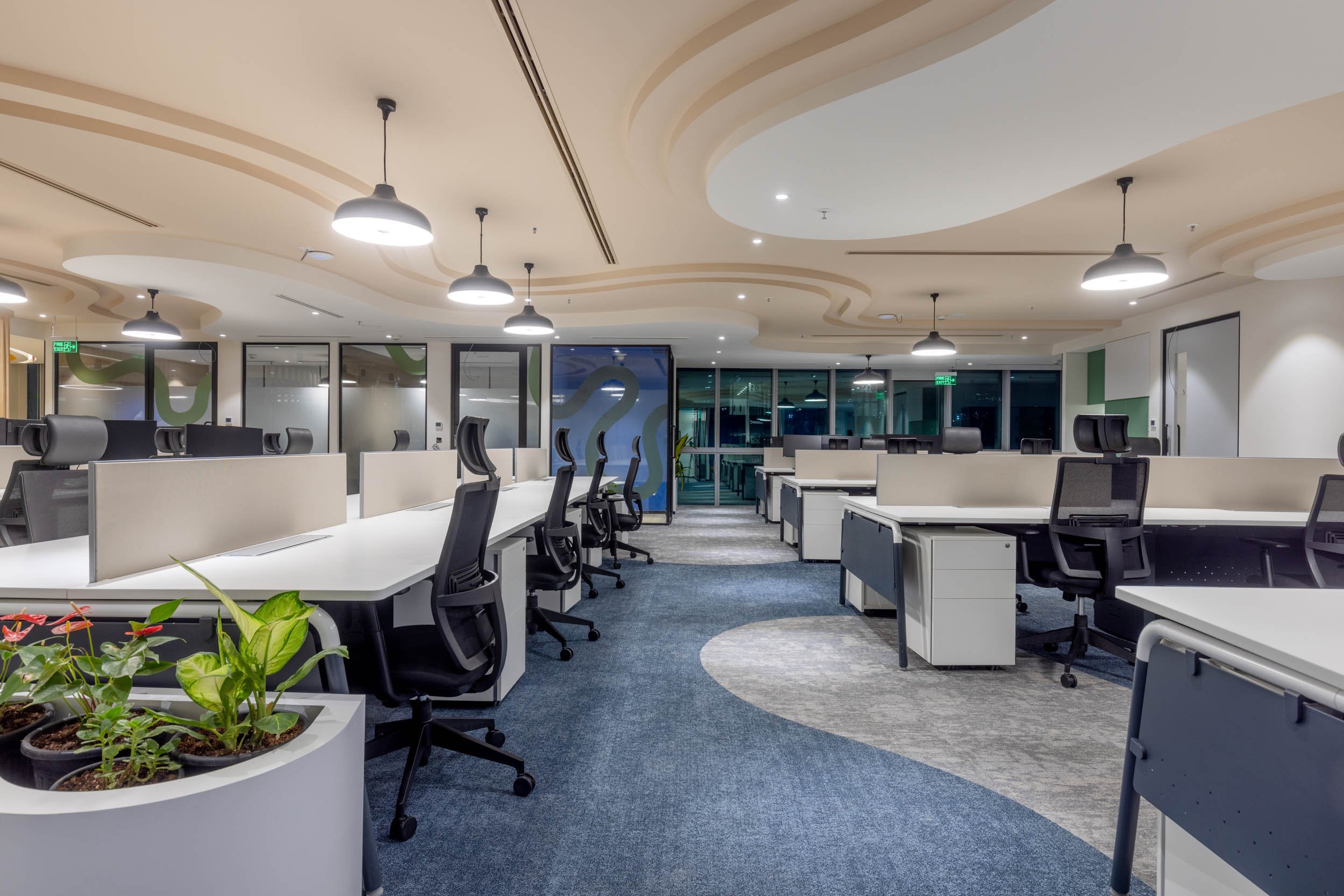 Commercial interior photography showcasing a modern corporate workspace, highlighting open-plan desk arrangements, biophilic office design, and a custom architectural curved wood ceiling