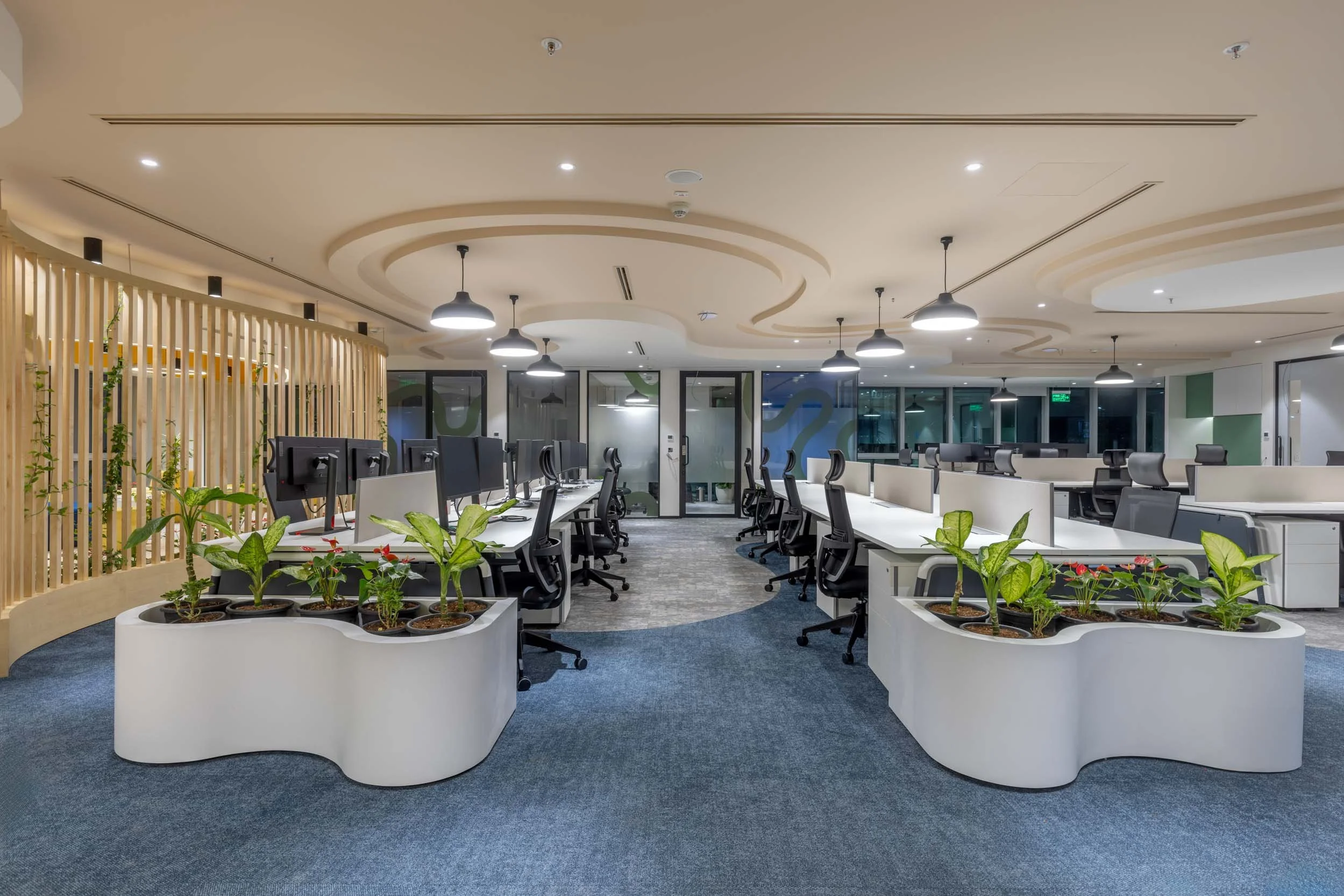 Commercial interior photography showcasing biophilic office design, highlighting custom serpentine planters, open-plan desk arrangements, and contemporary workspace lighting.