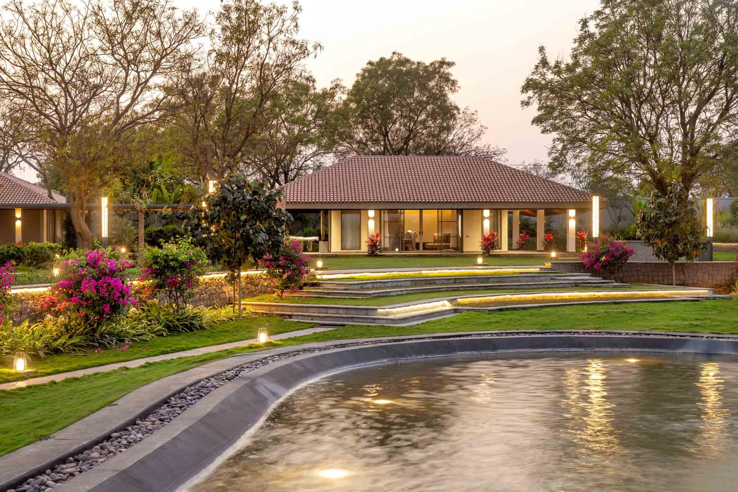 Twilight landscape photography of a luxury residential estate featuring a curved swimming pool, manicured lawns, and warm exterior lighting