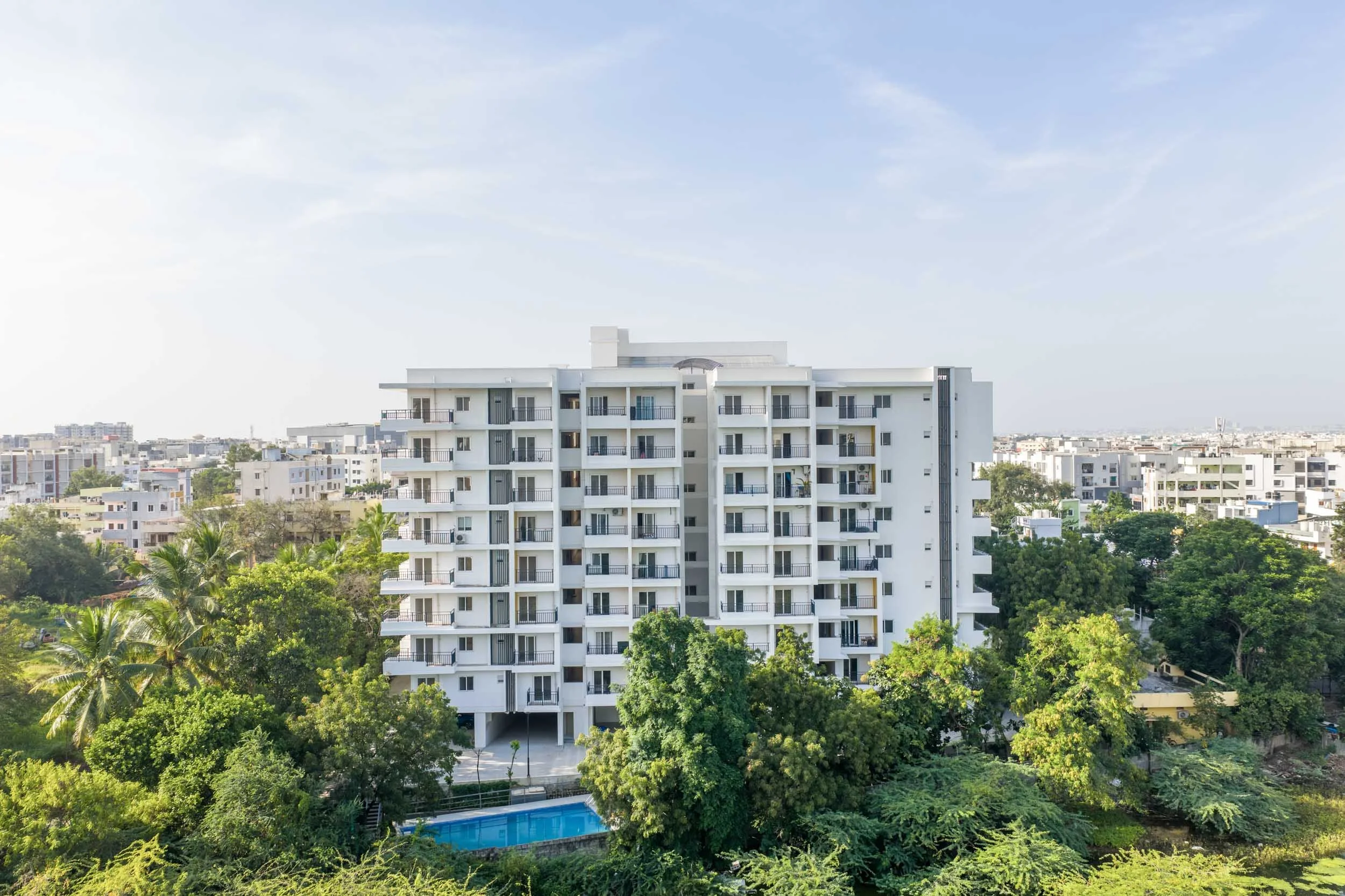 Exterior real estate photography featuring a modern white apartment building surrounded by mature trees and abundant natural green spaces